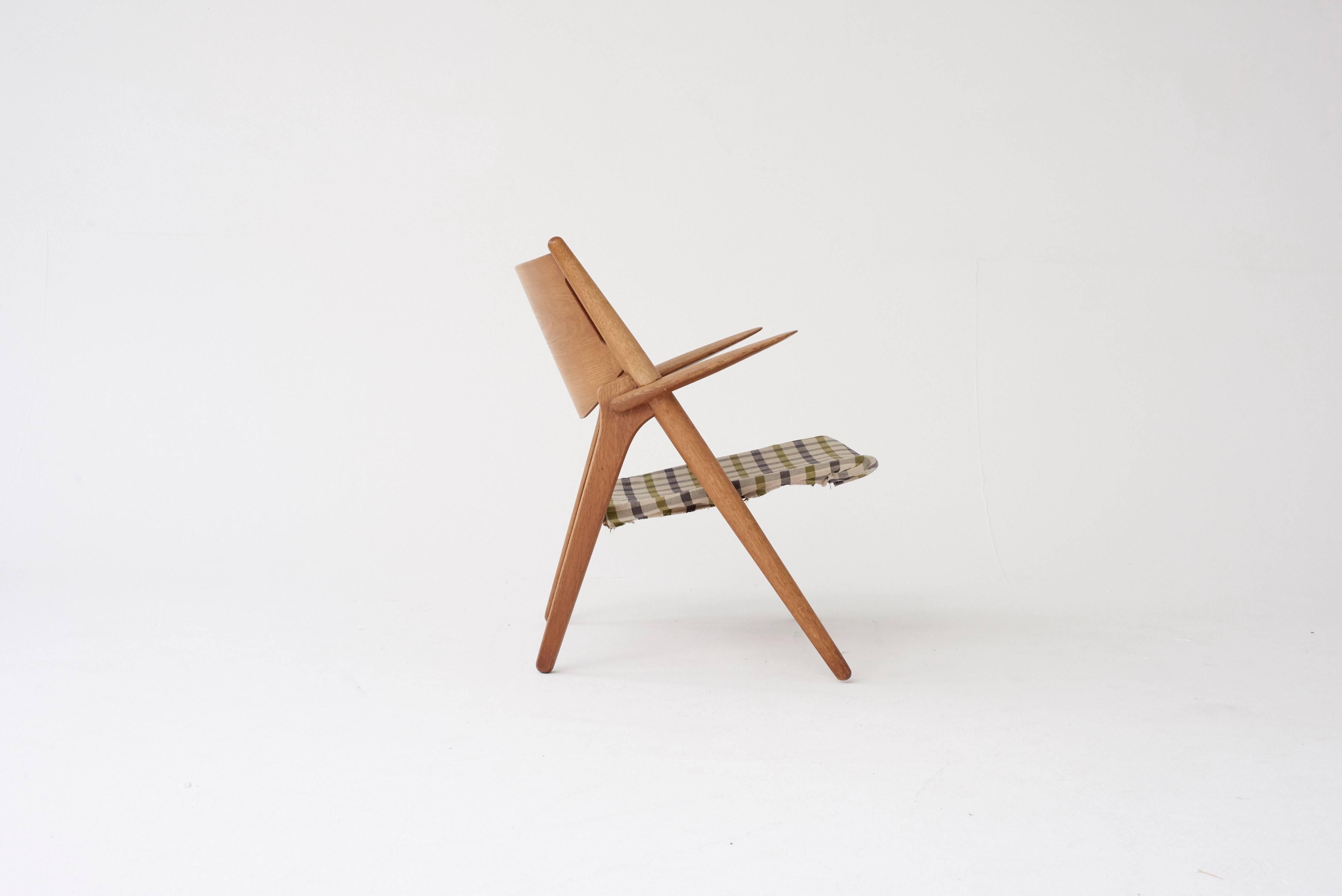 A super early and original example of the classic Hans Wegner CH-28 sawbuck armchair. Oak frame, with lovely grain, and fabric seat. Price includes recovering of seat in customer supplied fabric or leather.