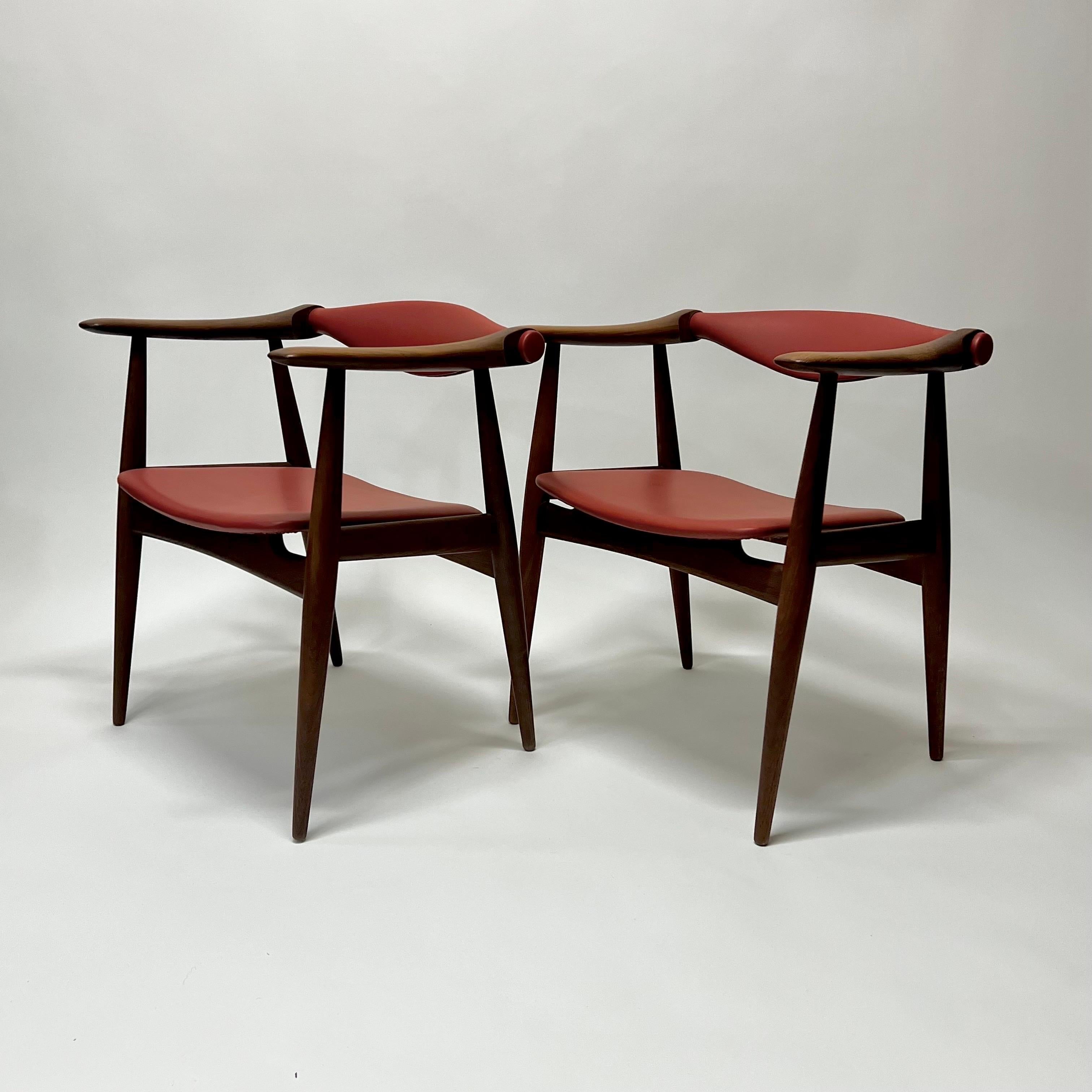 Rare and stunning model CH32 armchairs in red leather by iconic designer, Hans Wegner. Solid teak frame with tapered legs and a rotating seat back for optimal comfort. Manufactured by Illums Bolighus. These chairs were purchased from Van Morrison.