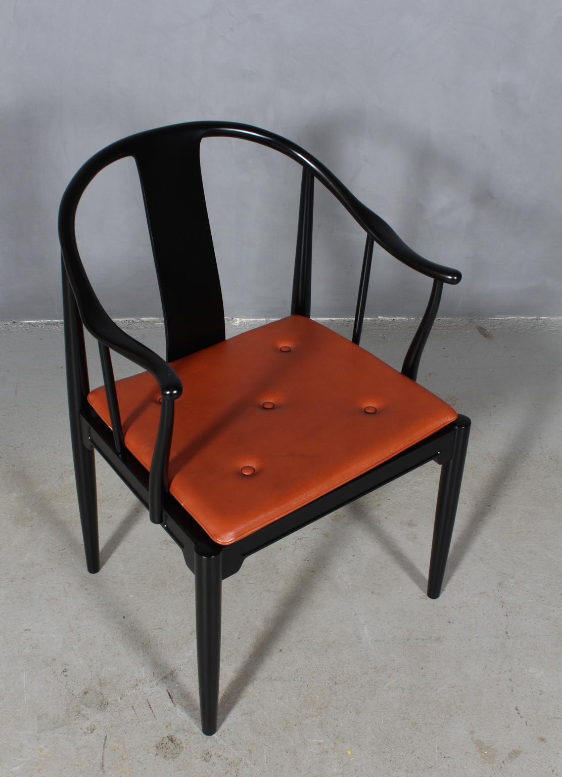 Hans J. Wegner famous and beautiful chair is an adaptation of an old Chinese chair of the Ming dynasty; “China Chair”. A very comfortable armchair made in newly lacquered black wood. Loose seat cushions upholstered with patinated tan leather, fitted