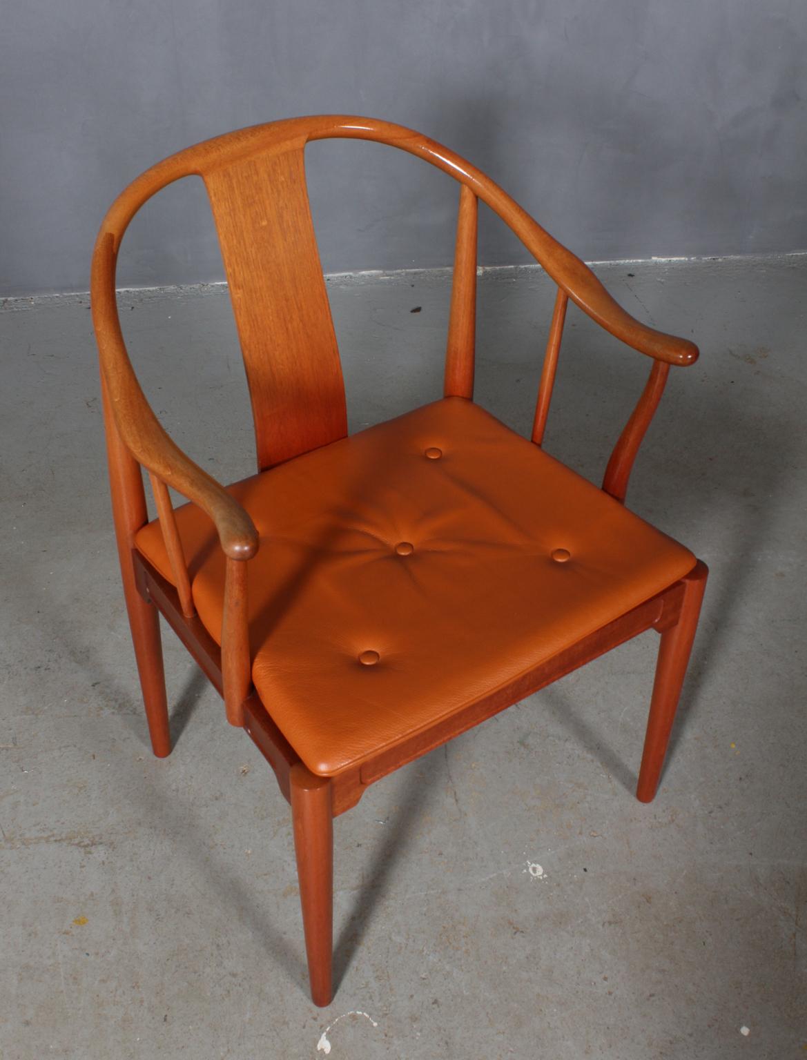 Hans J. Wegner famous and beautiful chair is an adaptation of an old Chinese chair of the Ming dynasty; “China Chair”. A very comfortable armchair made in mahogany. Loose seat cushions upholstered with patinated tan leather, fitted with buttons.