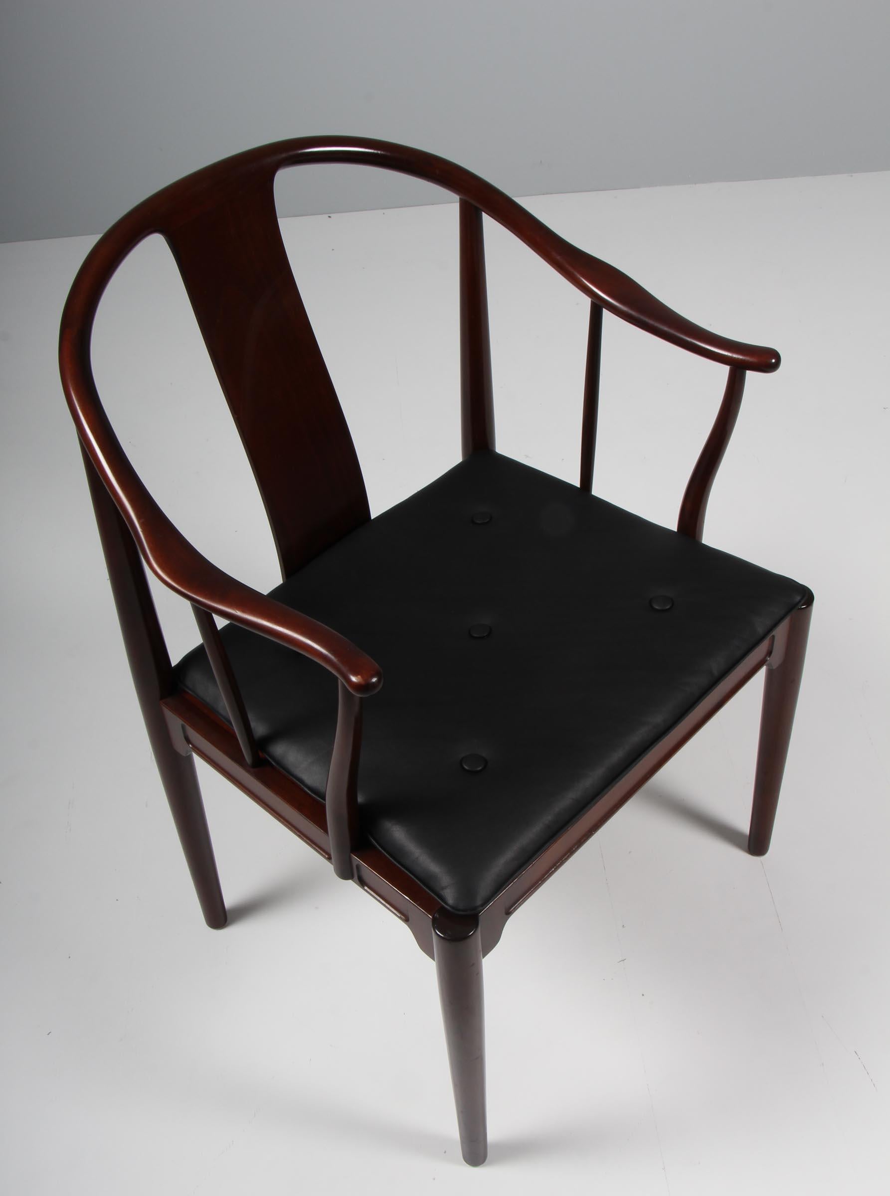 Hans J. Wegner famous and beautiful chair is an adaptation of an old Chinese chair of the Ming dynasty; “China Chair”. A very comfortable armchair made in mahogany. Loose seat cushions new upholstered with black aniline leather, fitted with buttons.