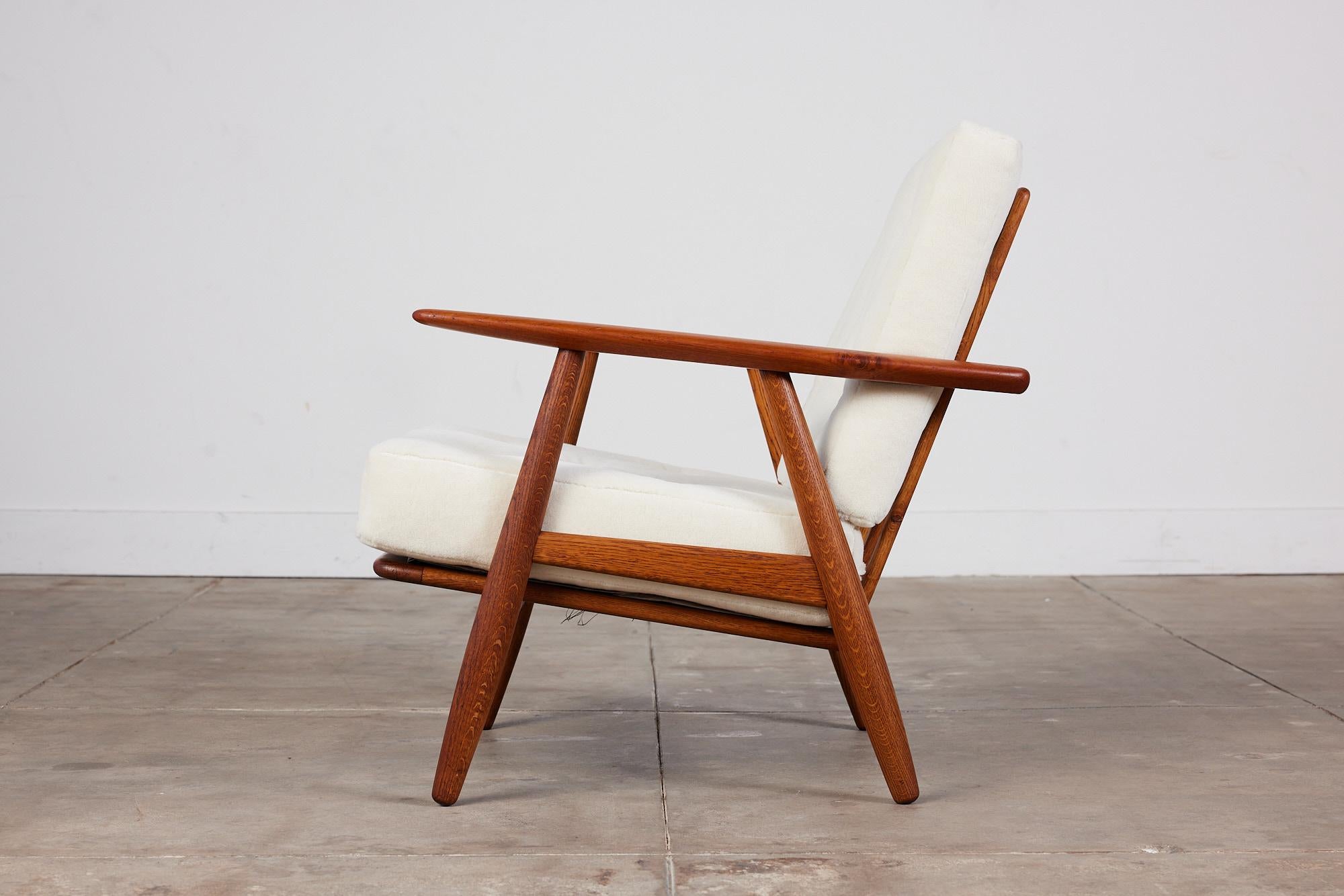 Lounge chair by Hans Wegner for Getama, c.1950s, Denmark. The chair features a solid teak and oak frame with vertical slatted back. The seat and back cushions have been replaced and are covered in a plush cream colored Italian alpaca velvet fabric