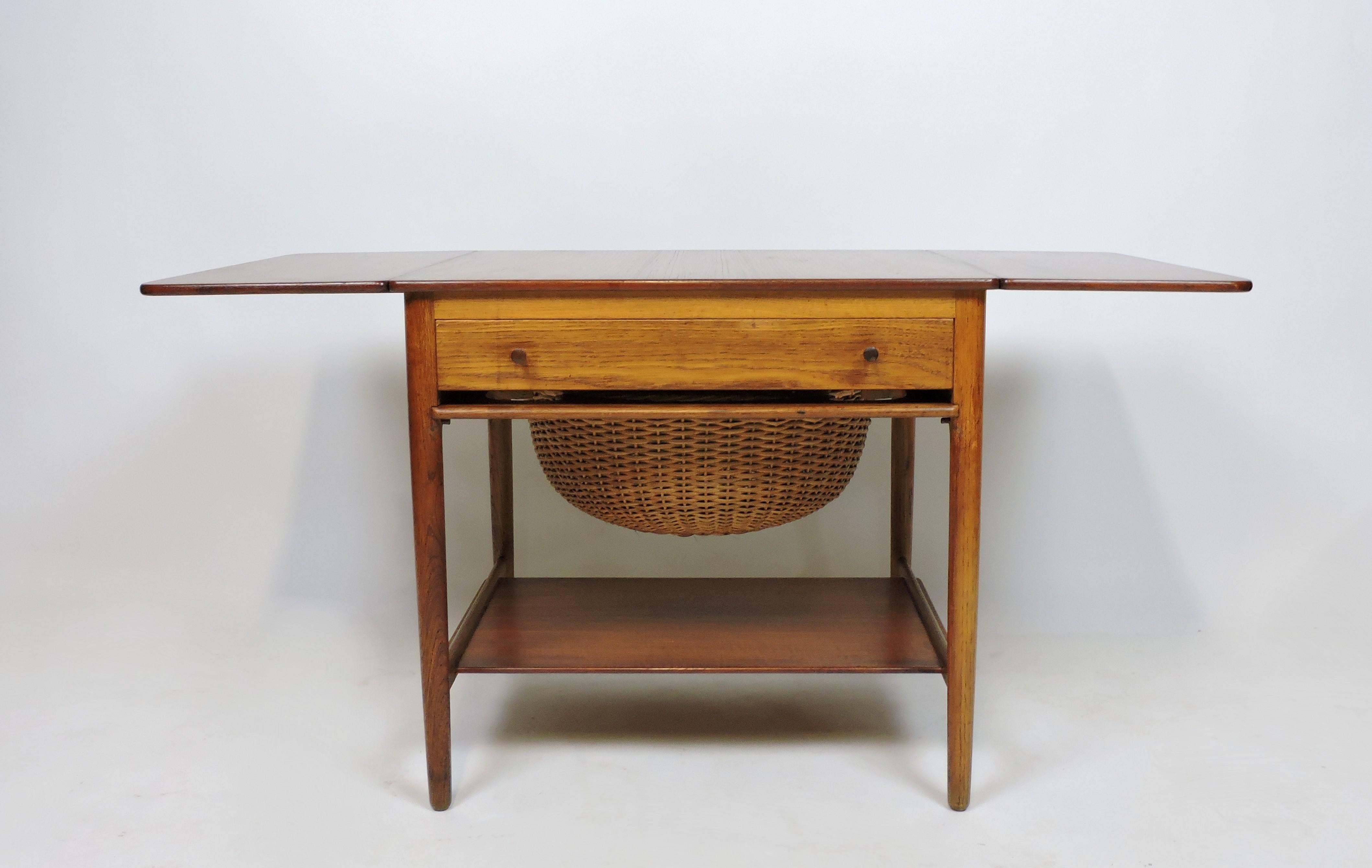Beautifully crafted early example of model AT-33 sewing table designed by Hans Wegner and manufactured in Denmark by cabinet maker, Andreas Tuck. This teak and oak table has two extendable side leaves, a drawer with compartments for sewing