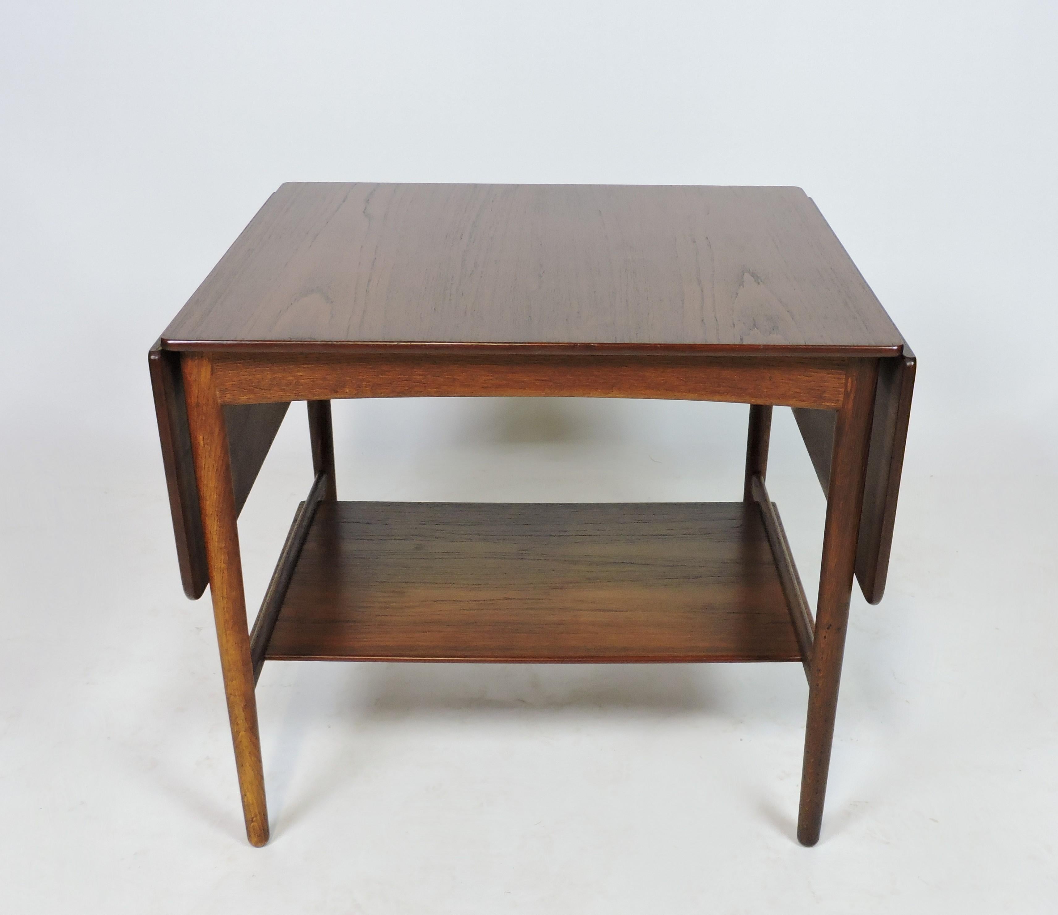 Beautifully crafted early example end or side table designed by Hans Wegner and manufactured in Denmark by cabinet maker, Andreas Tuck. This teak and oak table has two extendable side leaves and a lower shelf. The top extends to a large 47 5/8