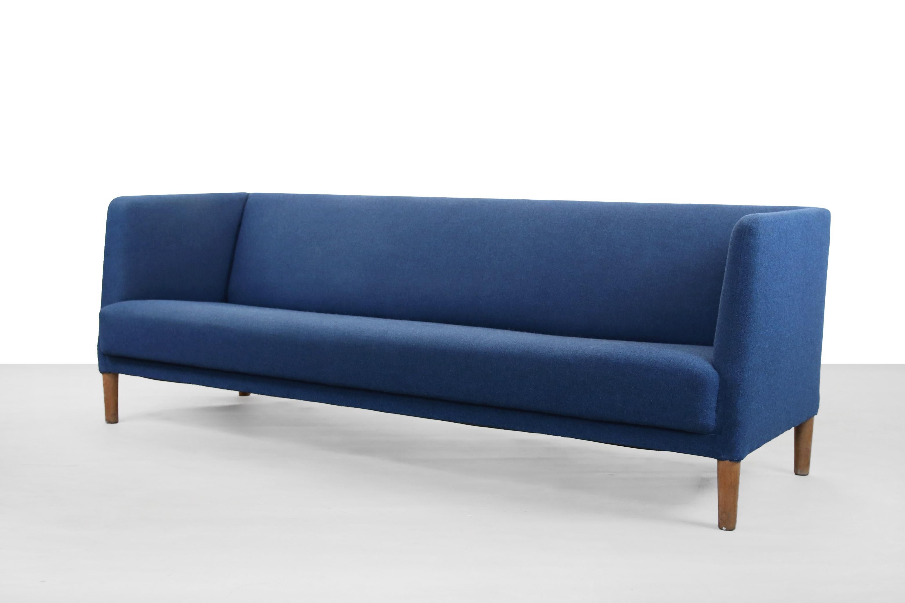 Danish modernist sofa designed by famous designer Hans J. Wegner and produced by Johannes Hansen in the 1950s in Denmark. The sofa has solid oak legs and is upholstered in blue wool fabric from Kvadrat Tonica 2 color 773. This beautiful sofa Model