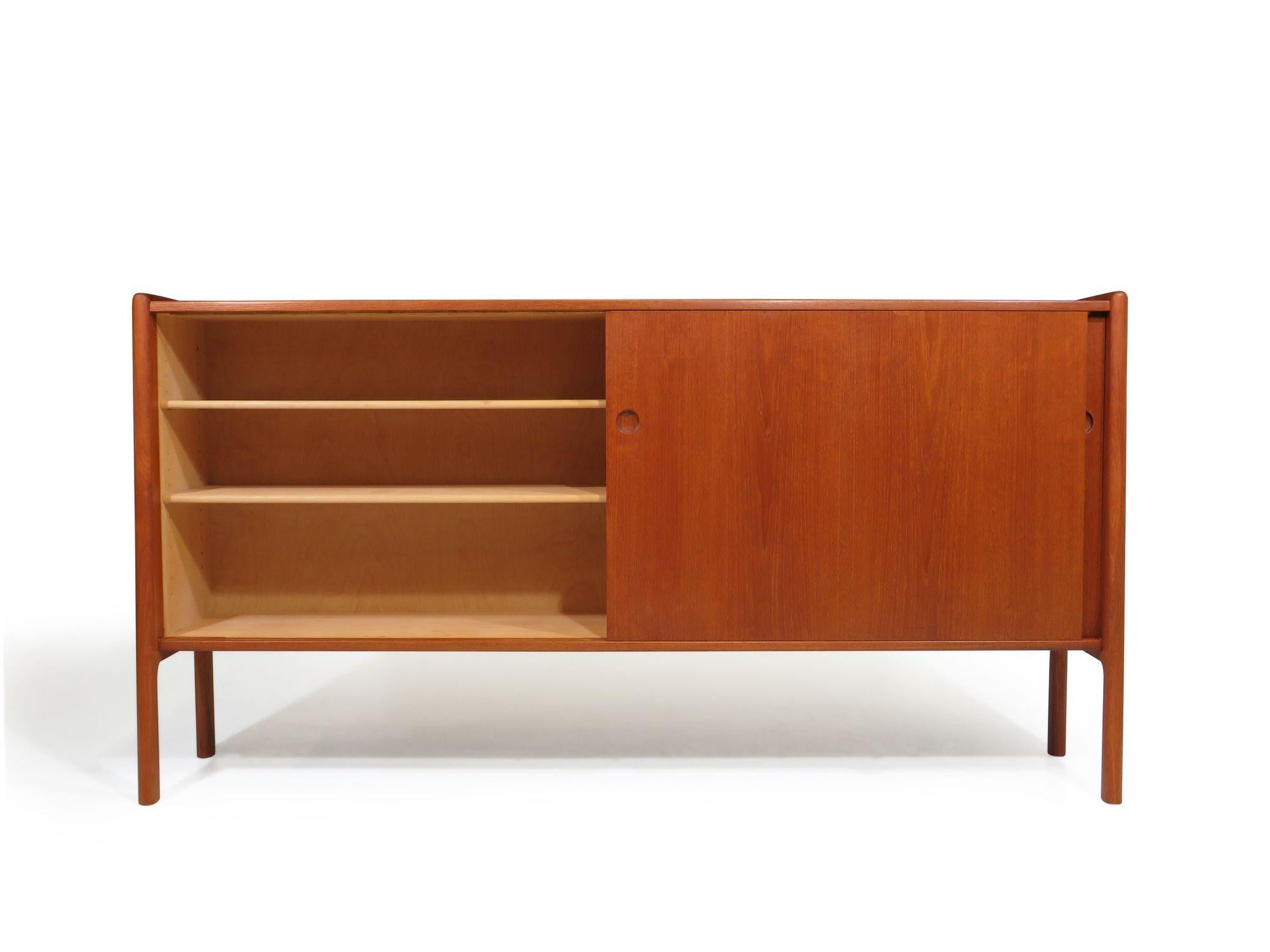 Teak credenza designed by Hans Wegner with two sliding doors revealing an interior of white oak with adjustable shelves; raised on solid teak legs. The cabinet has been professionally restored in a natural oil finish with minor signs of age and use.