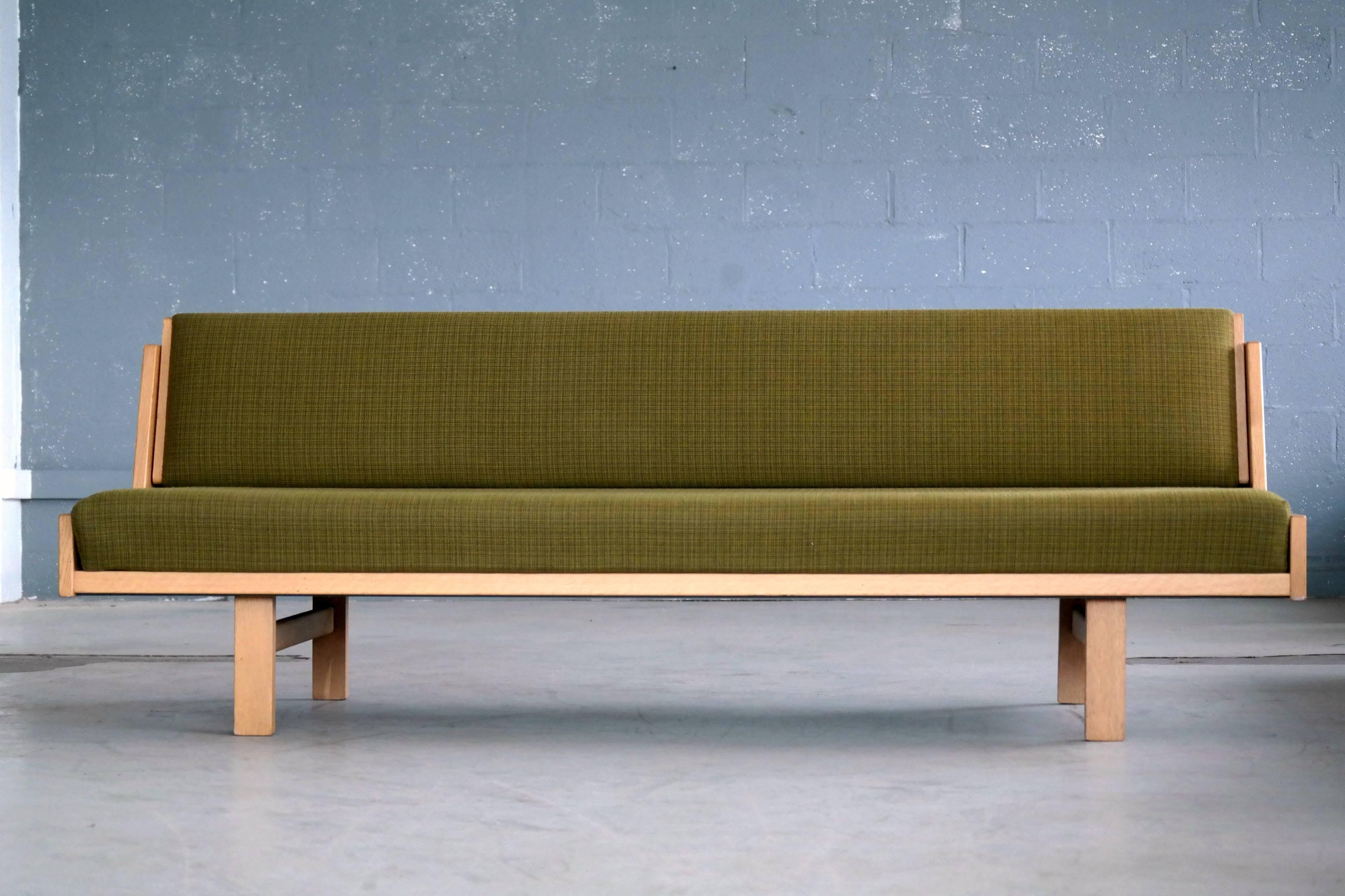 Hans Wegner's iconic daybed designed in 1954 and produced by GETAMA in Denmark. The daybed is made from oak veneer raised on solid oak legs and has it's original spring loaded mattress covered in a green wool by Kvadrat. The backrest which also