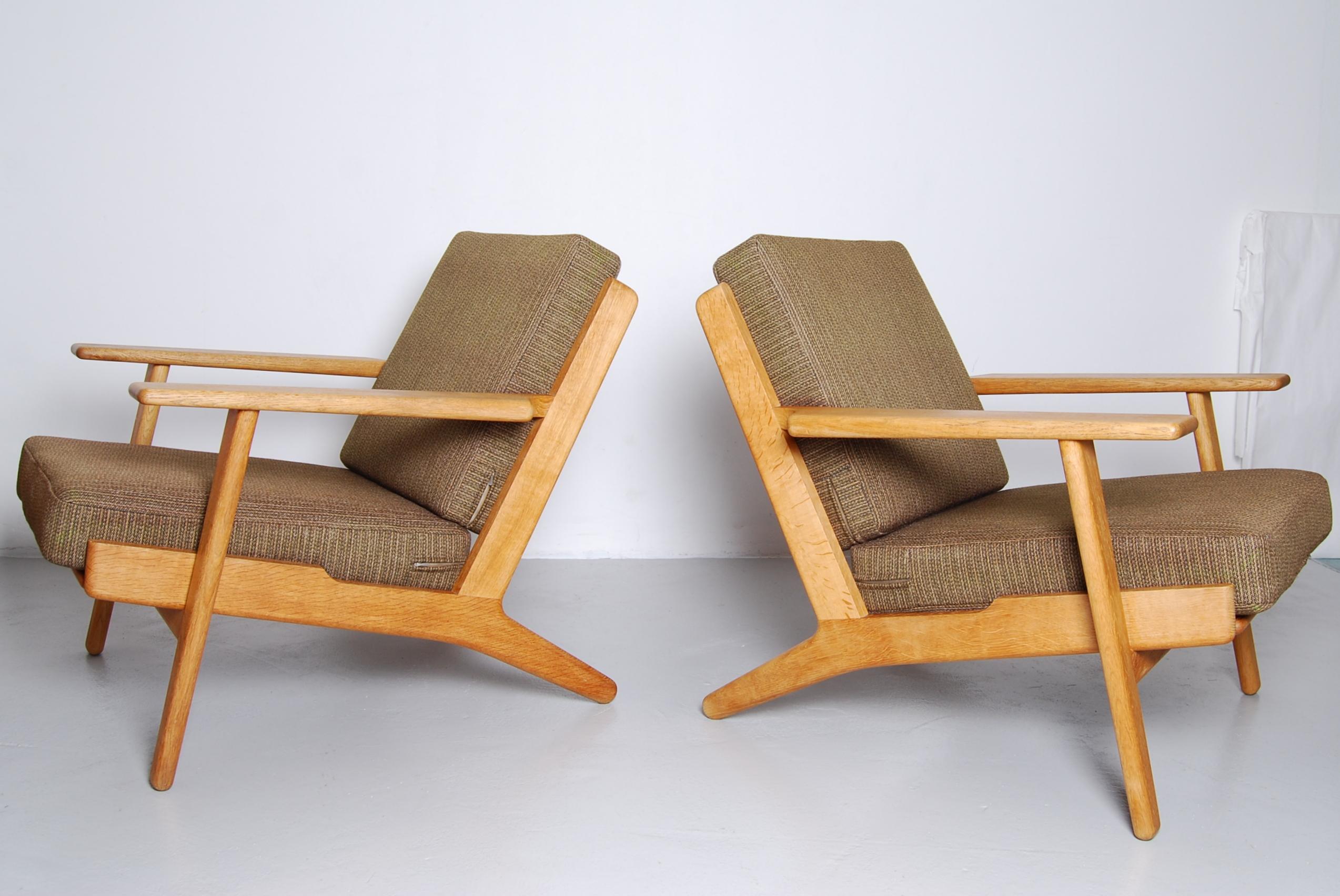 A pair of the Hans J Wegner GE290 lounge chairs. This early, original model was produced by GETAMA in Gedsted, Denmark. Oak frame in stunning condition with original Danish wool upholstery with natural signs of use and age. Original foam and metal