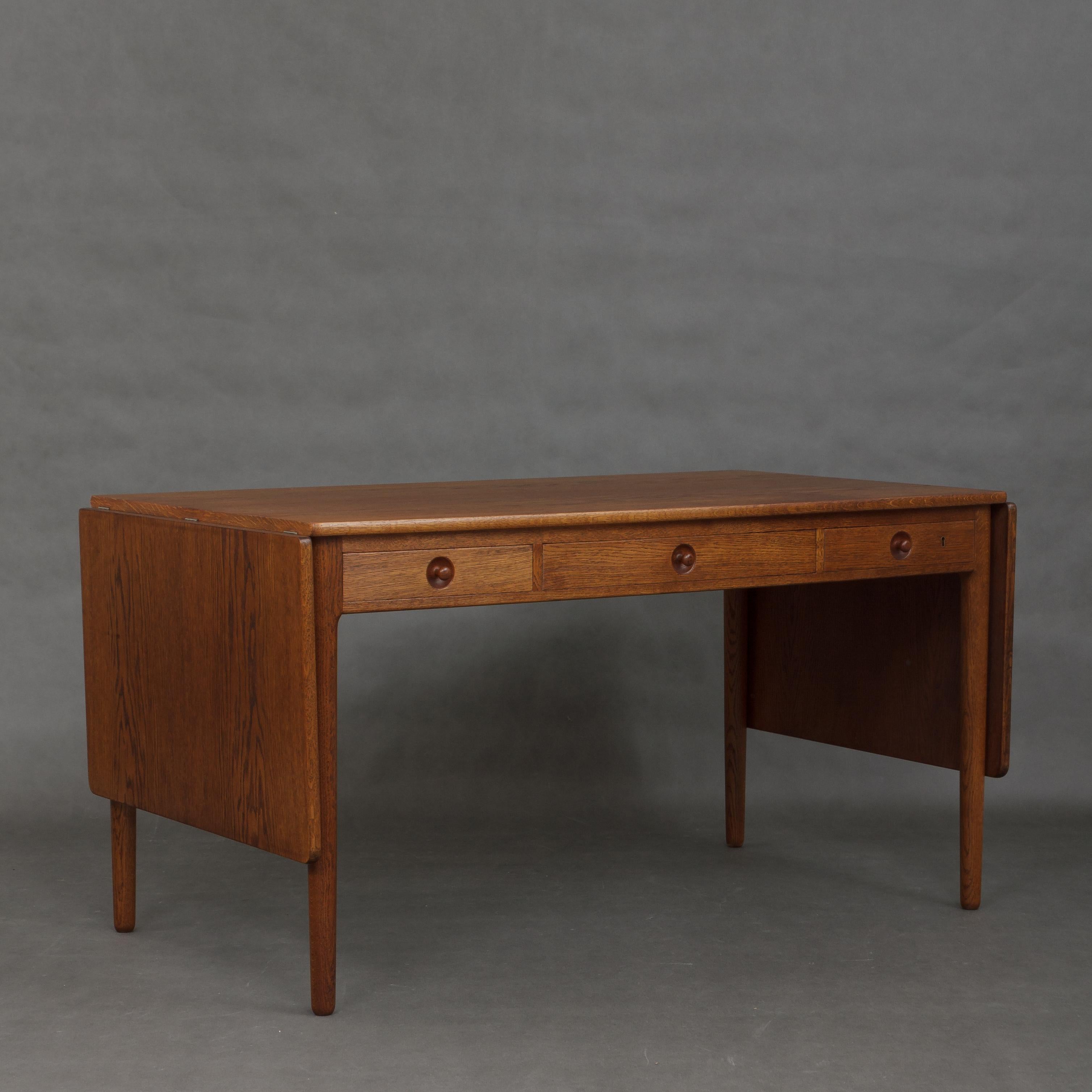 Designed in 1955 by Hans Wegner and manufactured by Andreas Tuck, this solid oak desk has two side leaves (55cm long each) with underneath support and three very deep drawers with organizers. Full length 246cm. This model comes from 1965y. And is in