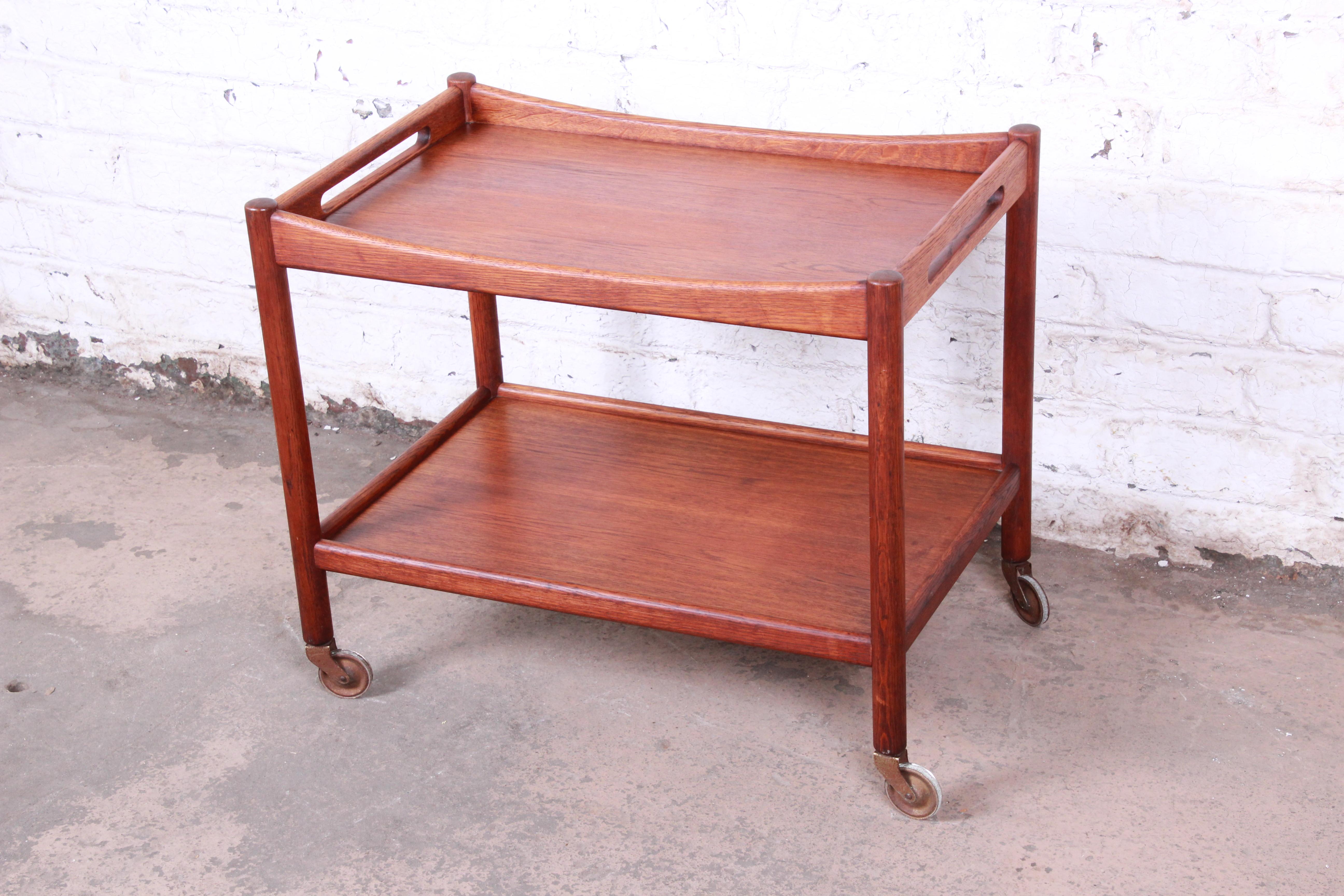 A rare midcentury Danish modern teak bar cart or serving trolley designed by Hans Wegner for Andreas Tuck. The cart features gorgeous teak wood grain and Minimalist Danish design. It sits on original casters for easy mobility. The original branded