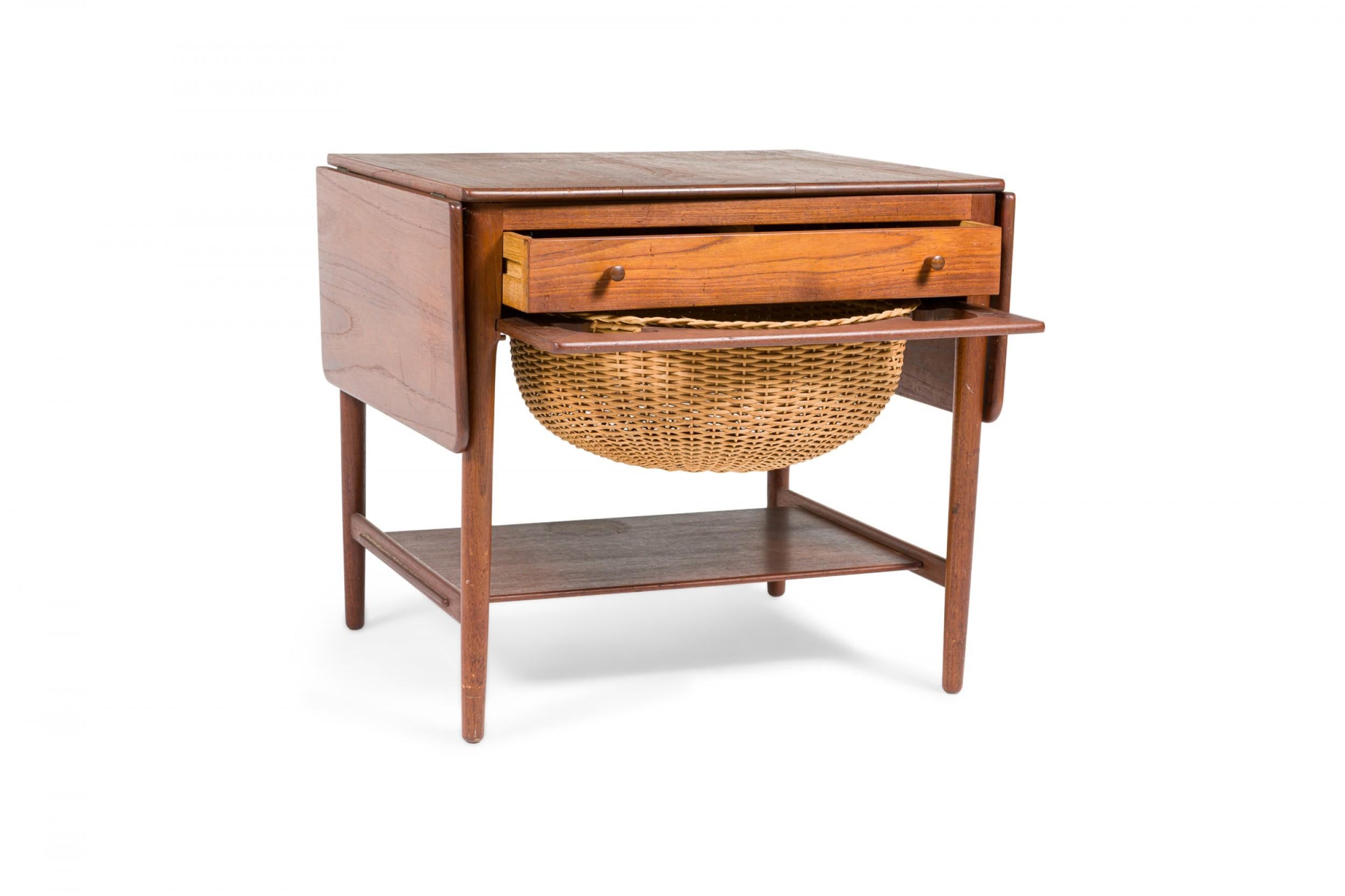 Danish Mid-Century teak drop leaf sewing table with a single drawer with two wooden drawer pulls and a wicker basket compartment mounted below the tabletop and above a lower stretcher shelf. (HANS WEGNER FOR ANDREAS TUCK)
