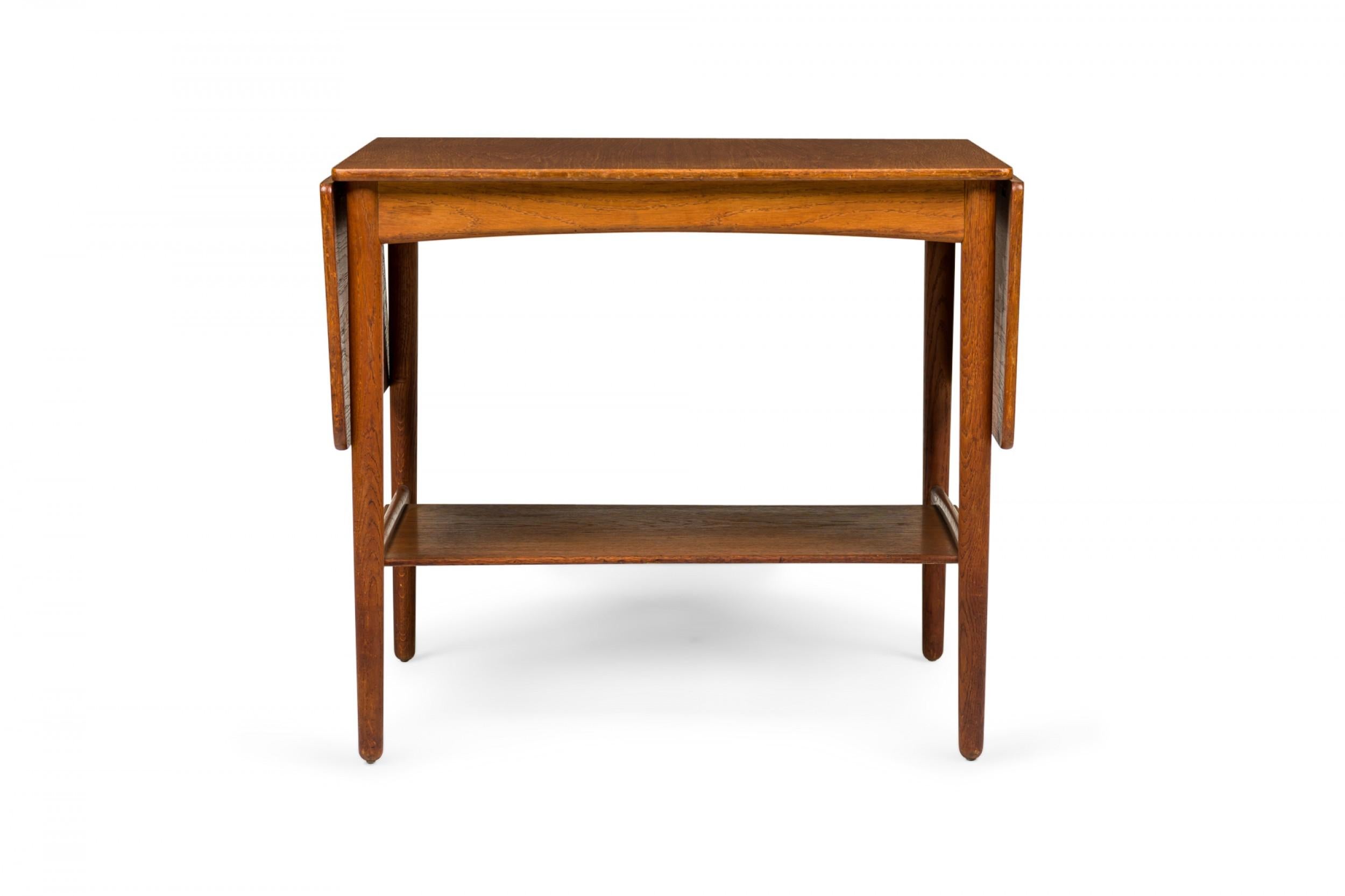 Danish mid-century wooden end / side table with a rectangular top and two drop leaves above a lower narrow stretcher shelf connecting four tapered dowel legs. (HANS WEGNER FOR ANDREAS TUCK)