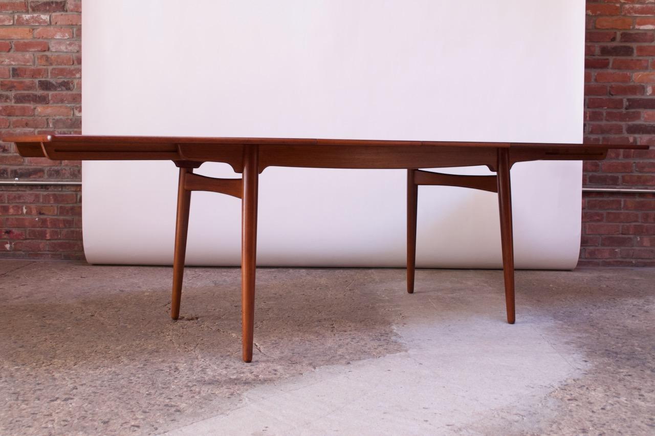 Model AT-310 teak dining table by Hans J. Wegner for Andreas Tuck, (Denmark, circa 1960). Composed of a teak surface supported by tapered, teak legs. Includes two additional 15.75