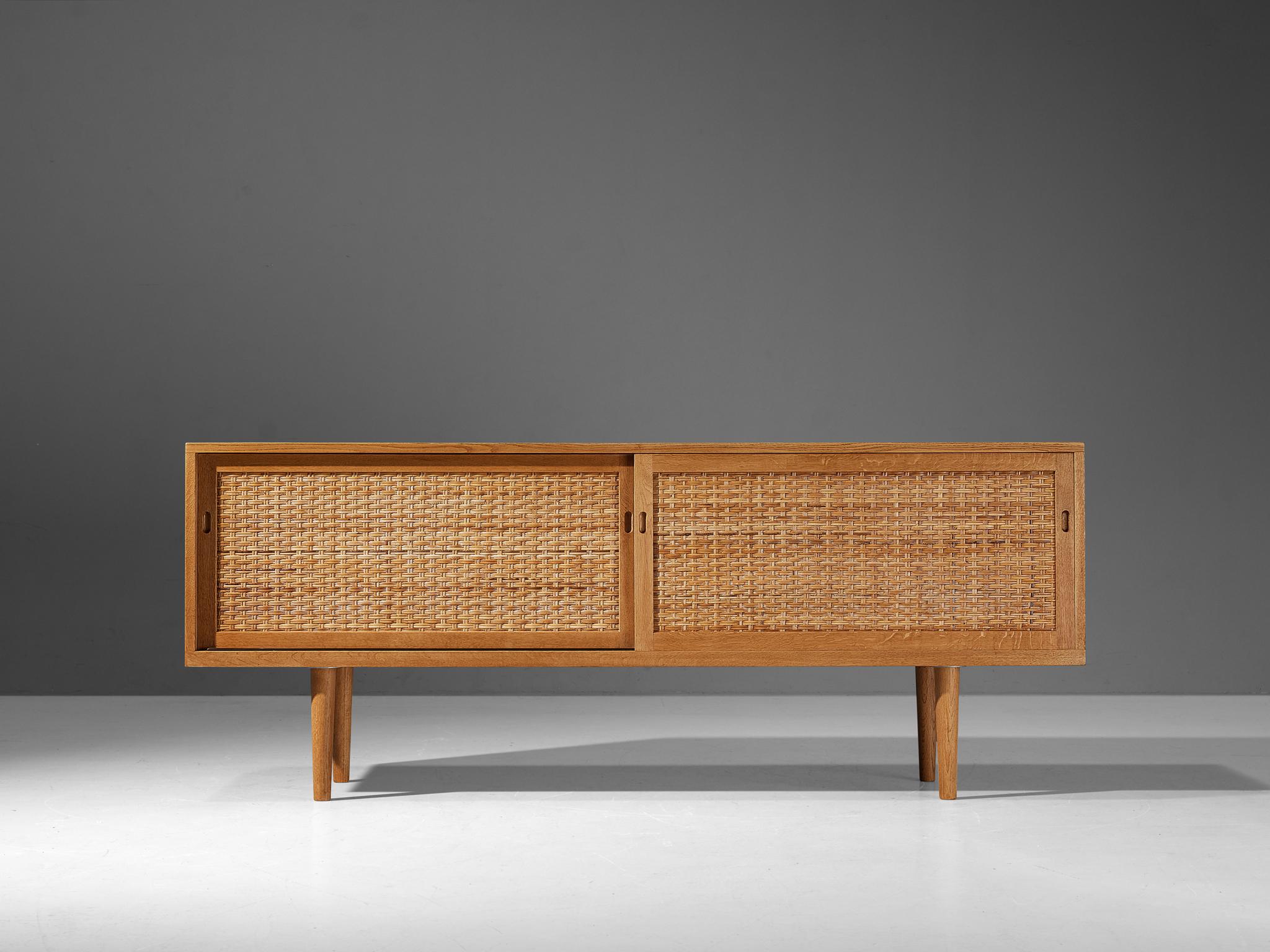 Hans J. Wegner for Ry Møbler, sideboard, oak, cane Denmark, ca. 1960 

A low sideboard that features fine, streamlined forms and is executed with honest, neutral materials. The corpus embodies a rectangular shape with clear lines and right-angled