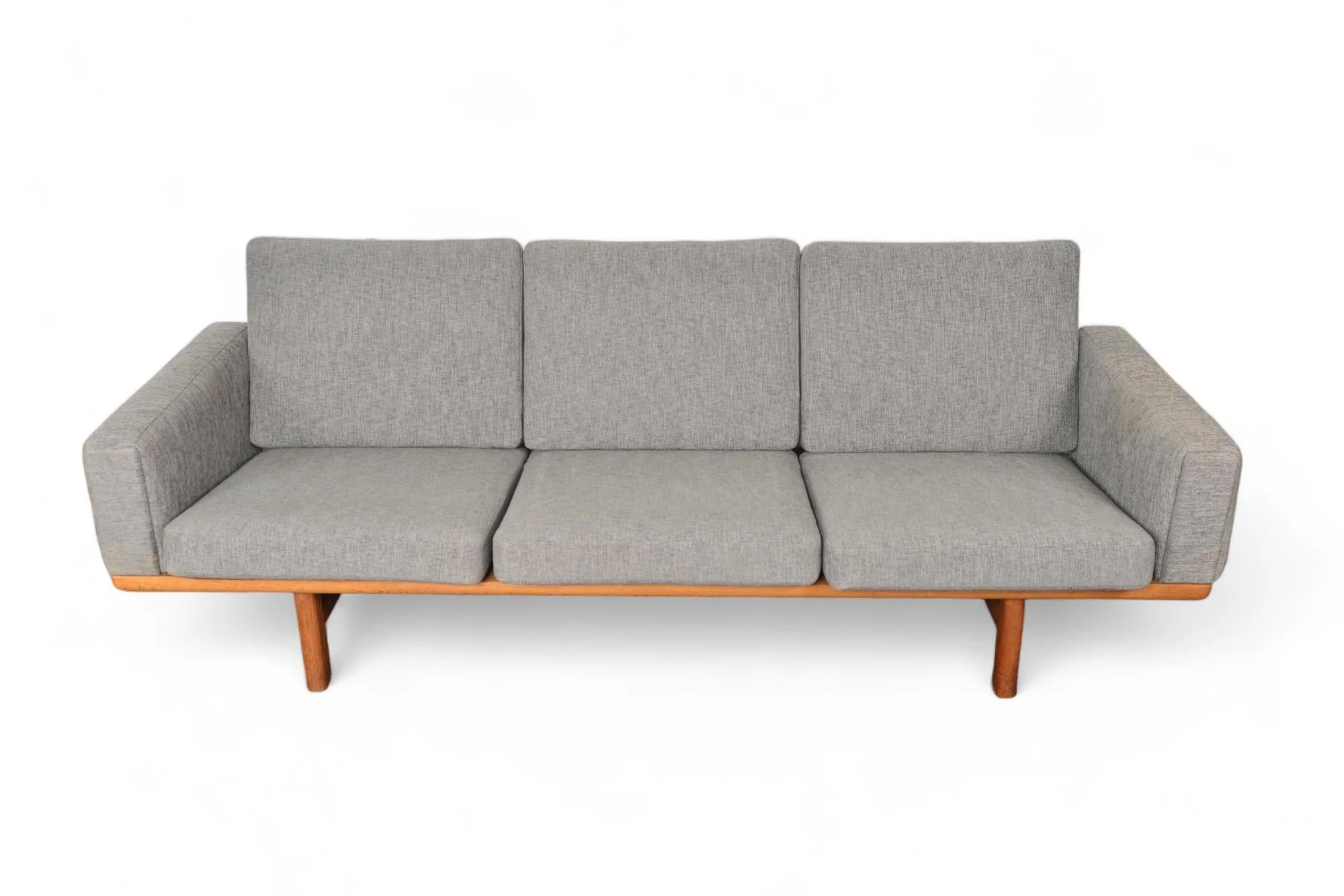This Danish modern three seat sofa in oak was designed by Hans Wegner as model GE- 236-3 for Getama in the 1950s. This excellently preserved piece showcases a sculptural back while providing upholstered arms and six original sprung cushions.