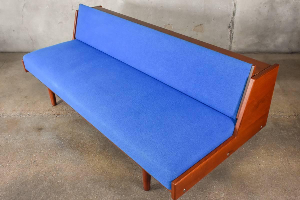 A convertible sofa/daybed designed by Hans J. Wegner for GETAMA, model 258. This example in teak with its original blue wool upholstery. The backrest lift up and back turning the sofa into a comfortable twin bed. Some slight discoloration to the