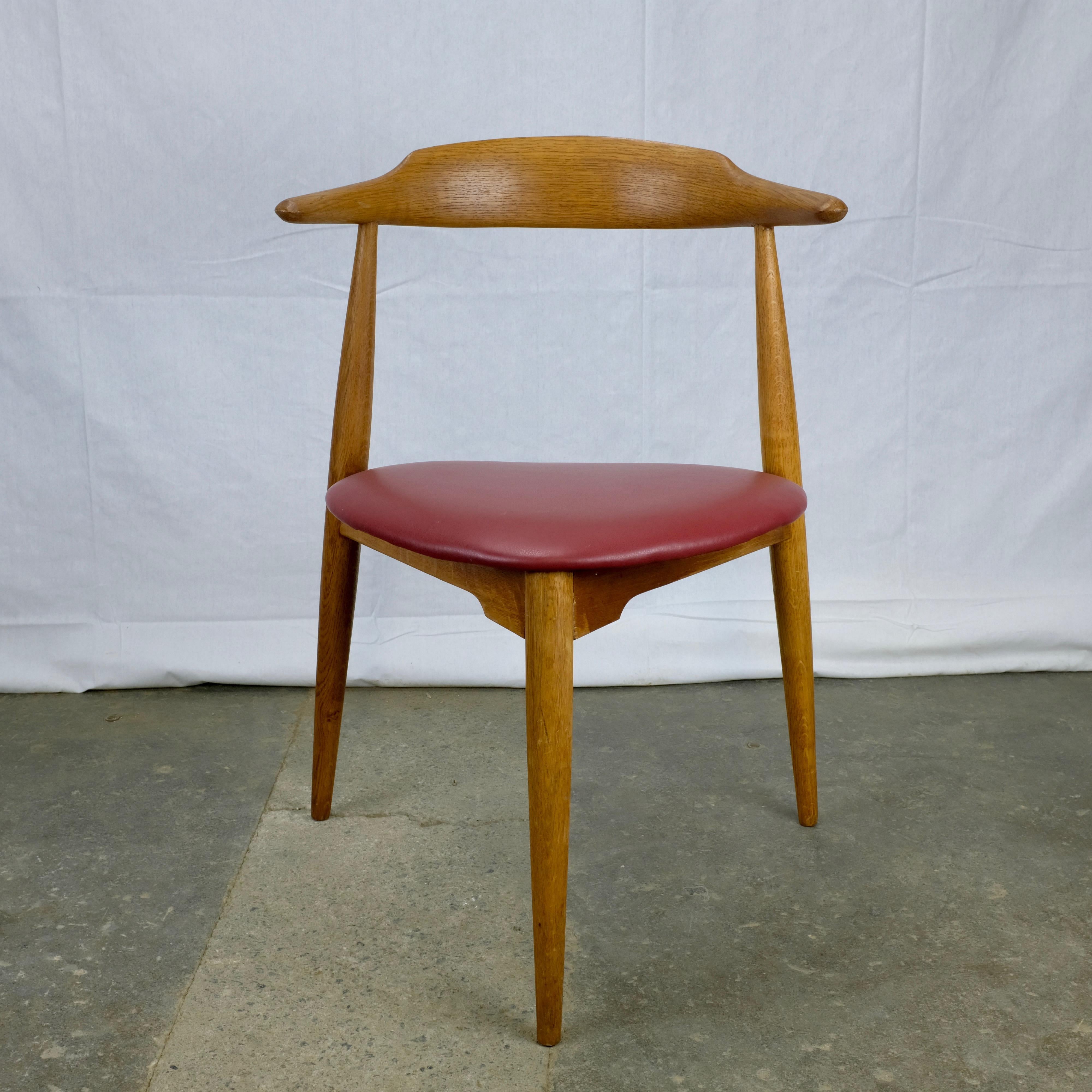Three-legged dining chair designed by Hans Wegner in 1953 and made in Denmark by Fritz Hansen. Known as the 'heart chair' for the shape of its seat.

Frame constructed in oak with red leatherette seat. Stamped with 'FH' and 'Denmark' across the