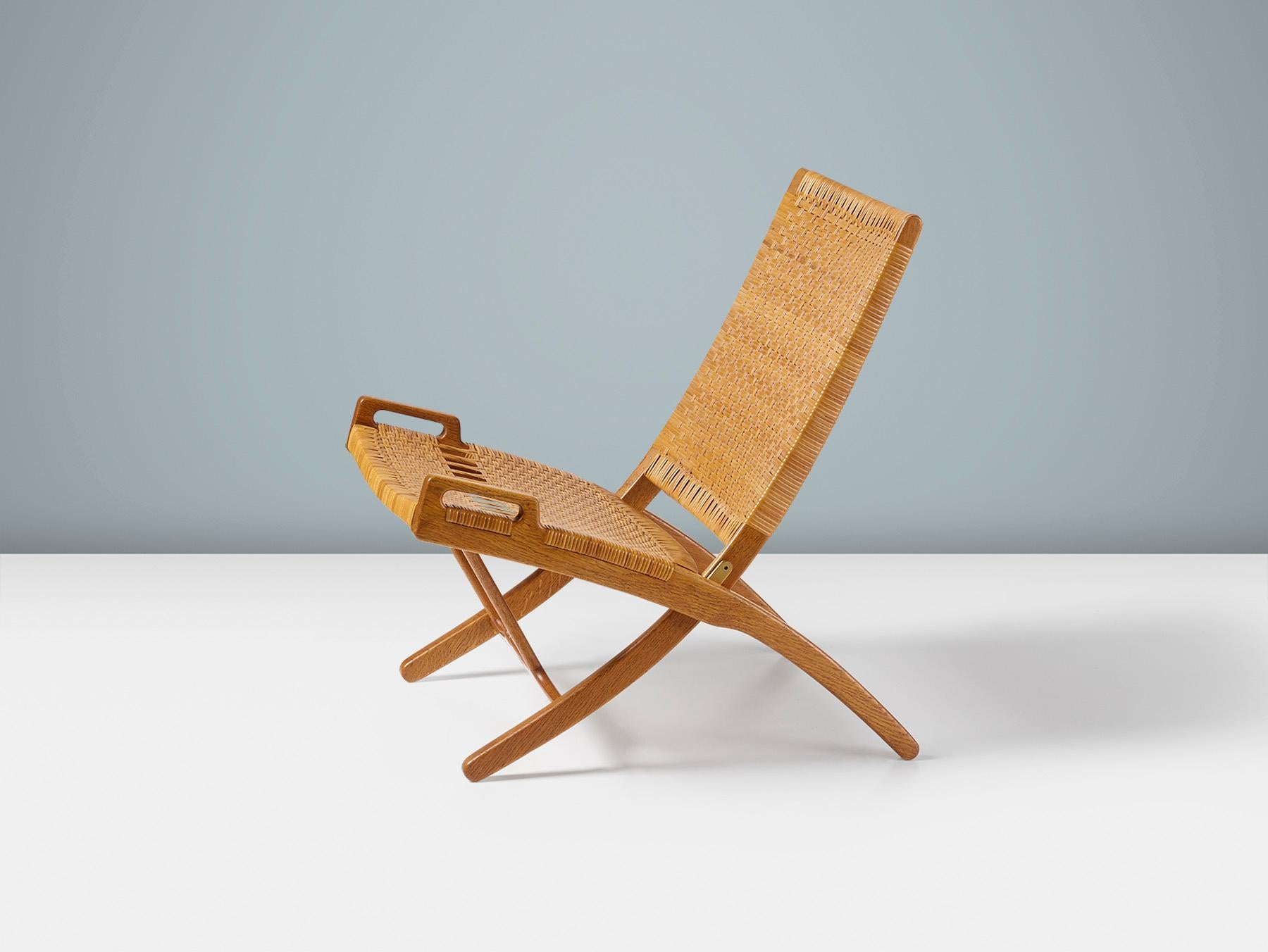 Esta clásica silla plegable de roble y caña fue una de las obras más importantes e icónicas del maestro danés Hans J. Wegner. La silla modelo 512 fue fabricada por el maestro ebanista Johannes Hansen en Copenhague durante su época dorada de