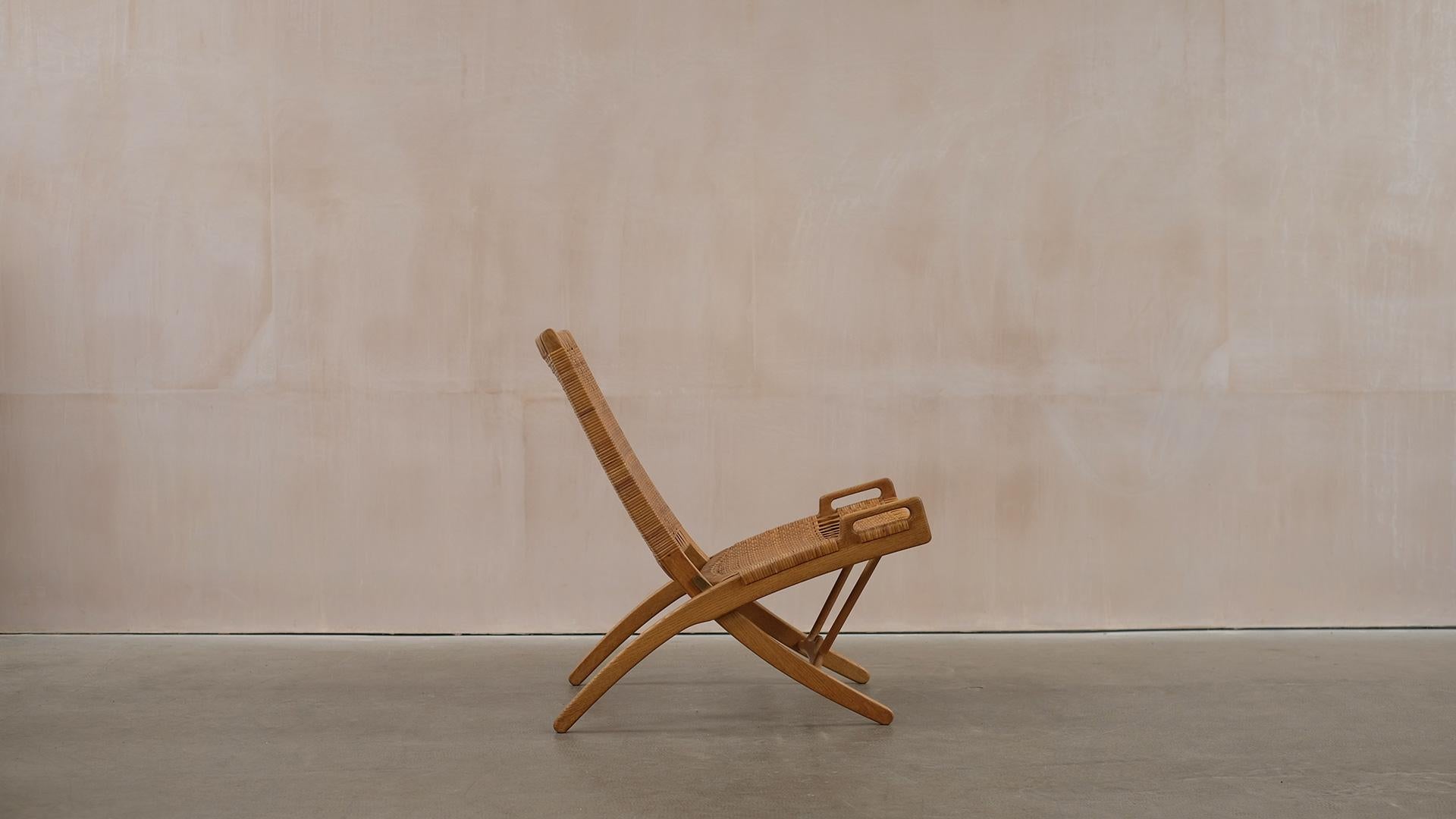 Folding chair in oak and cane designed by Hans Wegner for cabinetmaker Johannes Hansen model JH512, Denmark 1949.  Wonderful example with beautiful patina. The cane is in very nice condition with a few minor historic repairs but supportive and