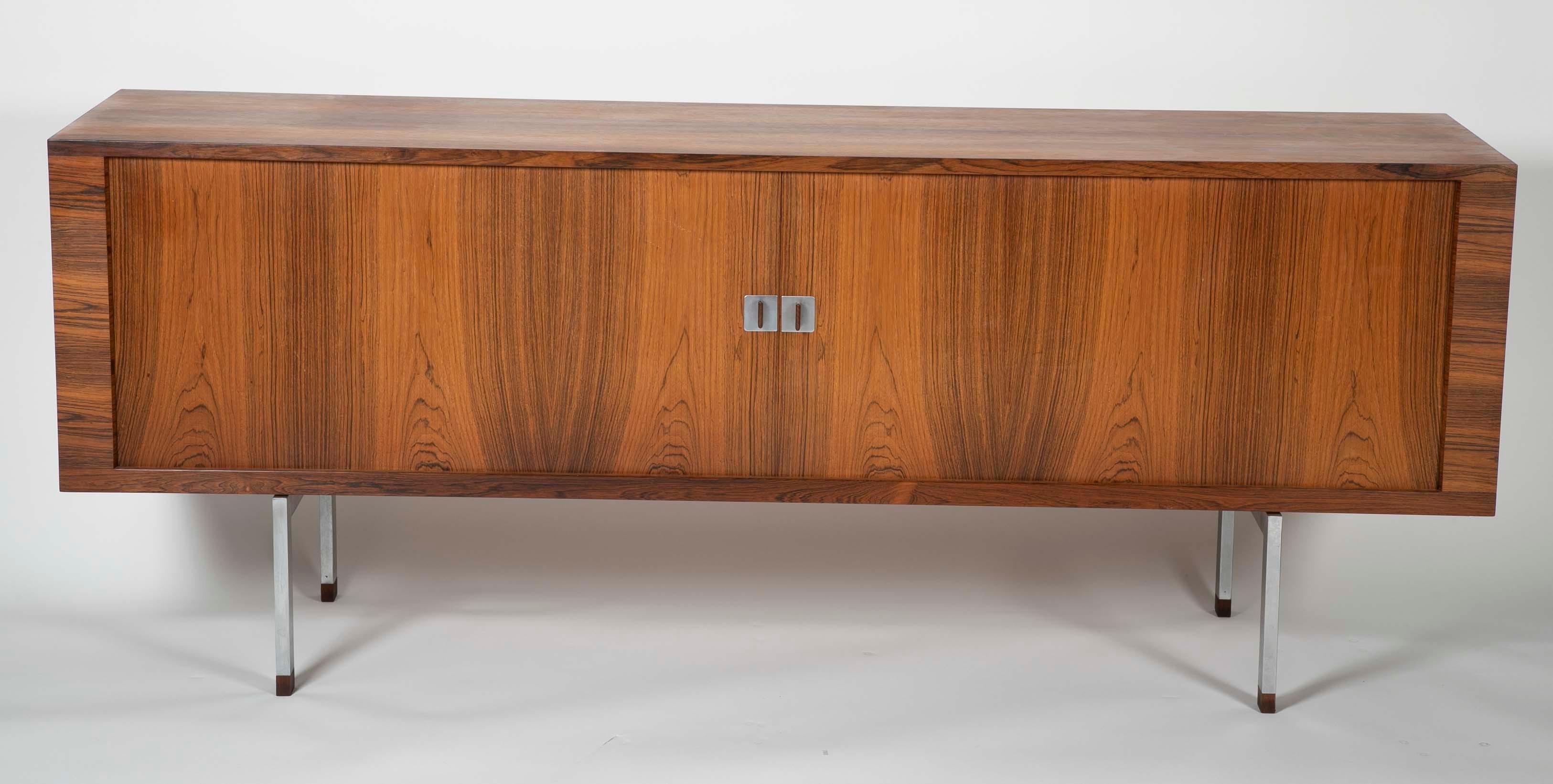 A Hans Wegner rosewood and white oak cabinet having a matte-chromed steel base. The cabinet opens using a pair of tambour doors. Manufactured by R&Y Mobler.
 