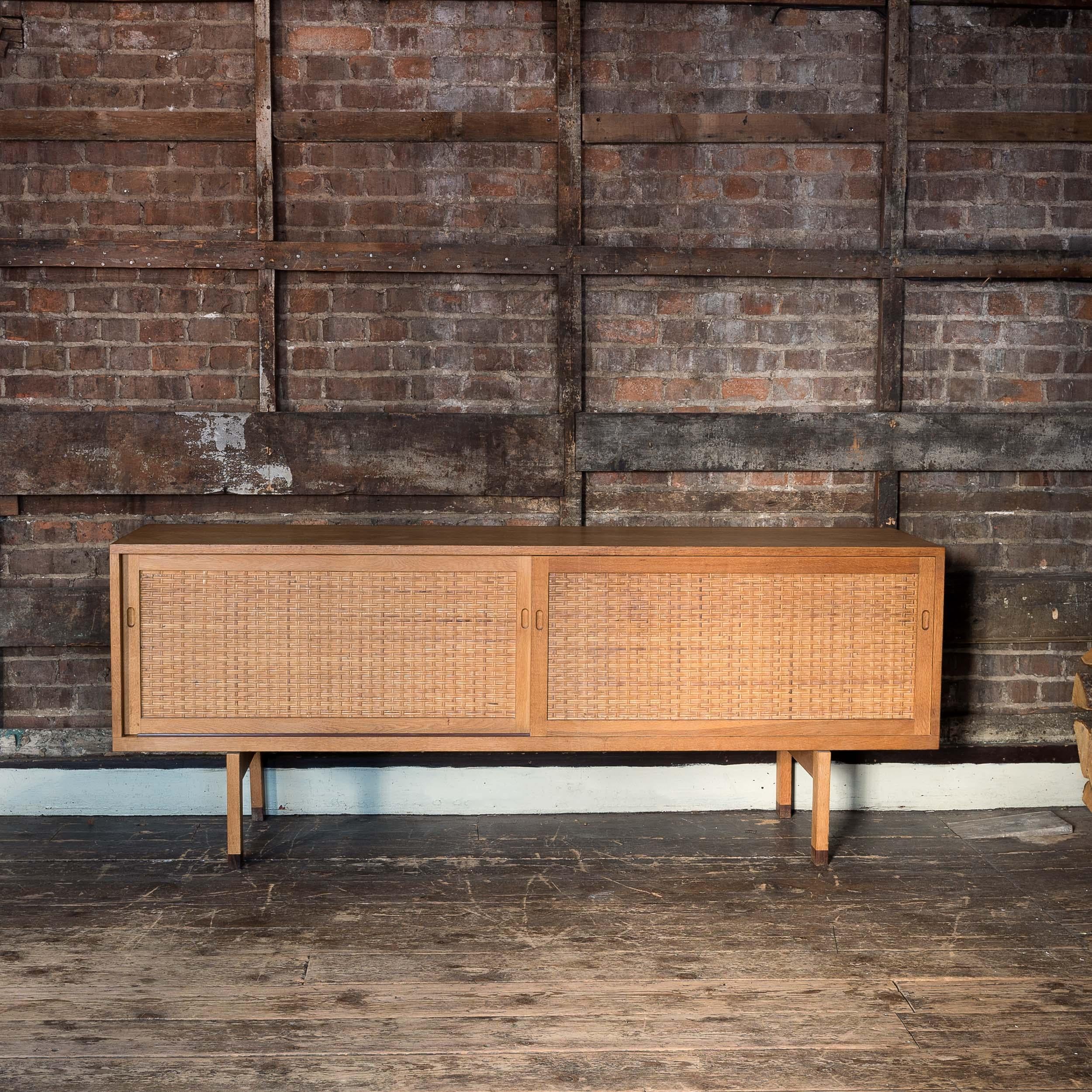 A Hans Wegner RY26 sideboard, manufactured by RY Møbler, mid-1950s.

Oak construction with rattan fronts to the sliding cabinet doors, the interior fitted with adjustable shelving and slides, with interior disc 'DANISH FURNITUREMAKERS CONTROL' .
