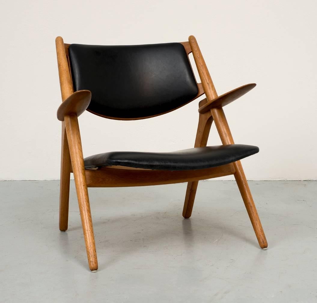 A fine example of Hans Wegner's CH-28 sawbuck lounge chair in oak and black leather. It is an iconic design that is at once sculptural, minimal and elegant. In excellent original condition.