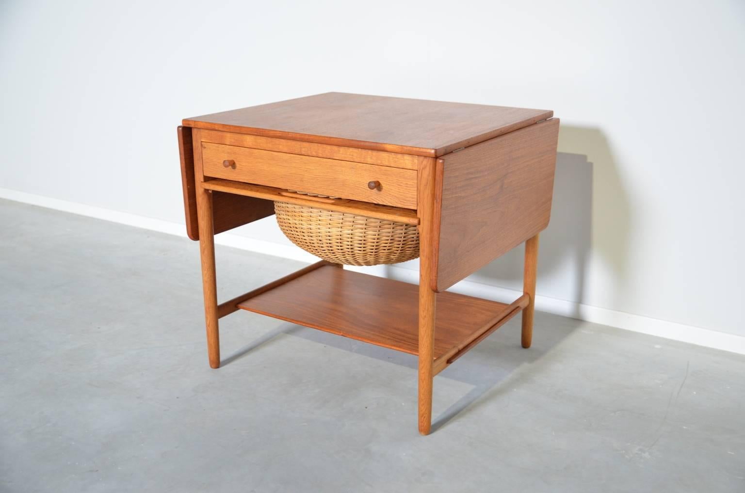 This sewing table (AT33) has a storage basket and a drawer with several compartments for storing yarn bobbins and other haberdashery. The table top can be extended by two drop-leafs, width 27 cm each.