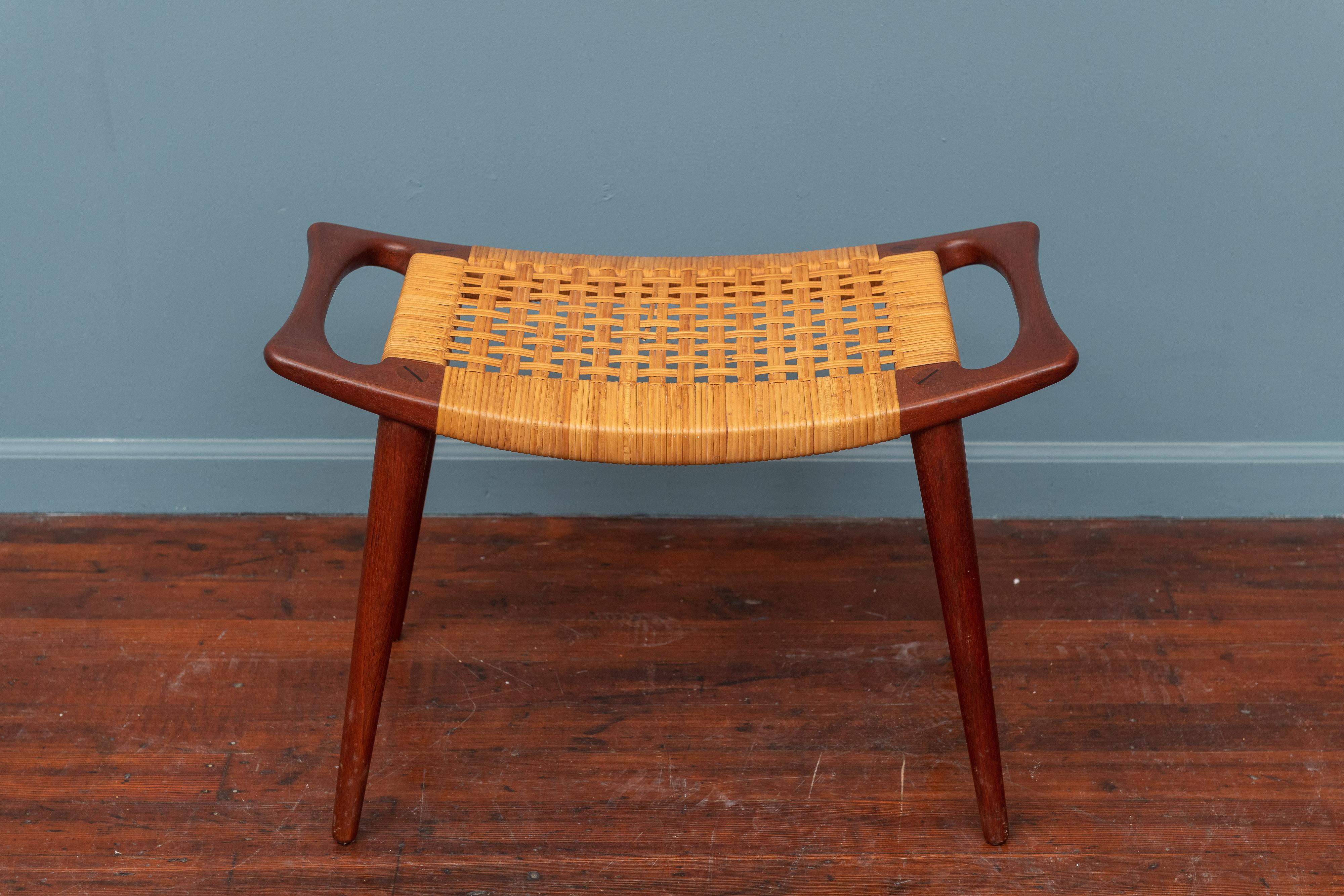 Hans Wegner design stool model JH539 made of sculpted teak with a cane seat, labeled. In excellent original condition, with two small breaks that have since been professionally repaired with new strands.