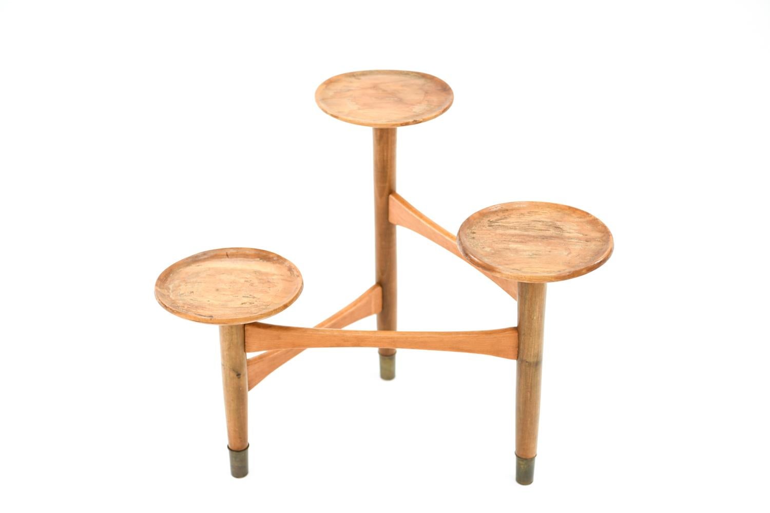 This Danish midcentury stand, circa 1950s. Made of beechwood with brass foot caps, this stand can be used to display planters or candles on its three tiers or used as a cake stand. An unusual little piece, rich with Scandinavian Modern flair.