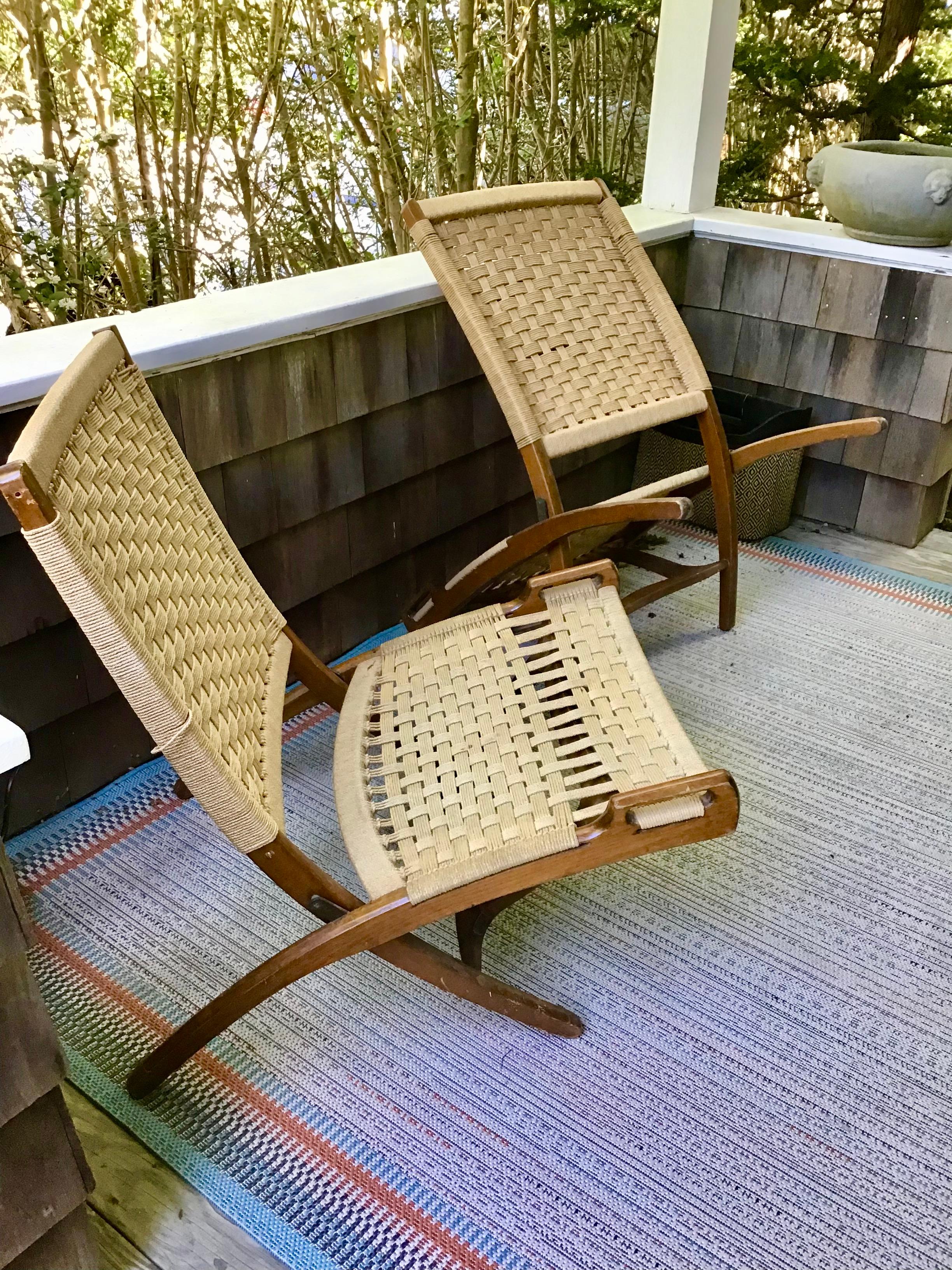 Pair of mid century Hans Wegner style folding chairs. Instead of cane, these seats are made of woven rope. The mid century chairs fold up easily and can be used in the yard, porch living room or beach. The Scandinavian modern chairs are in good