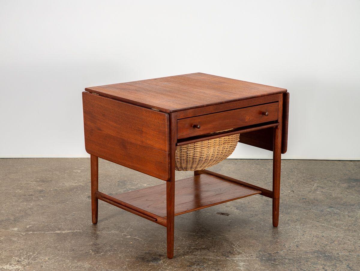 Danish Modern AT-33 sewing table, designed by Hans J. Wegner design for Andreas Tuck. A marvelous example of craftsmanship, this sewing table features drop leaves, a beautiful wicker basket, and deep drawer with spindles and divisions for thread and