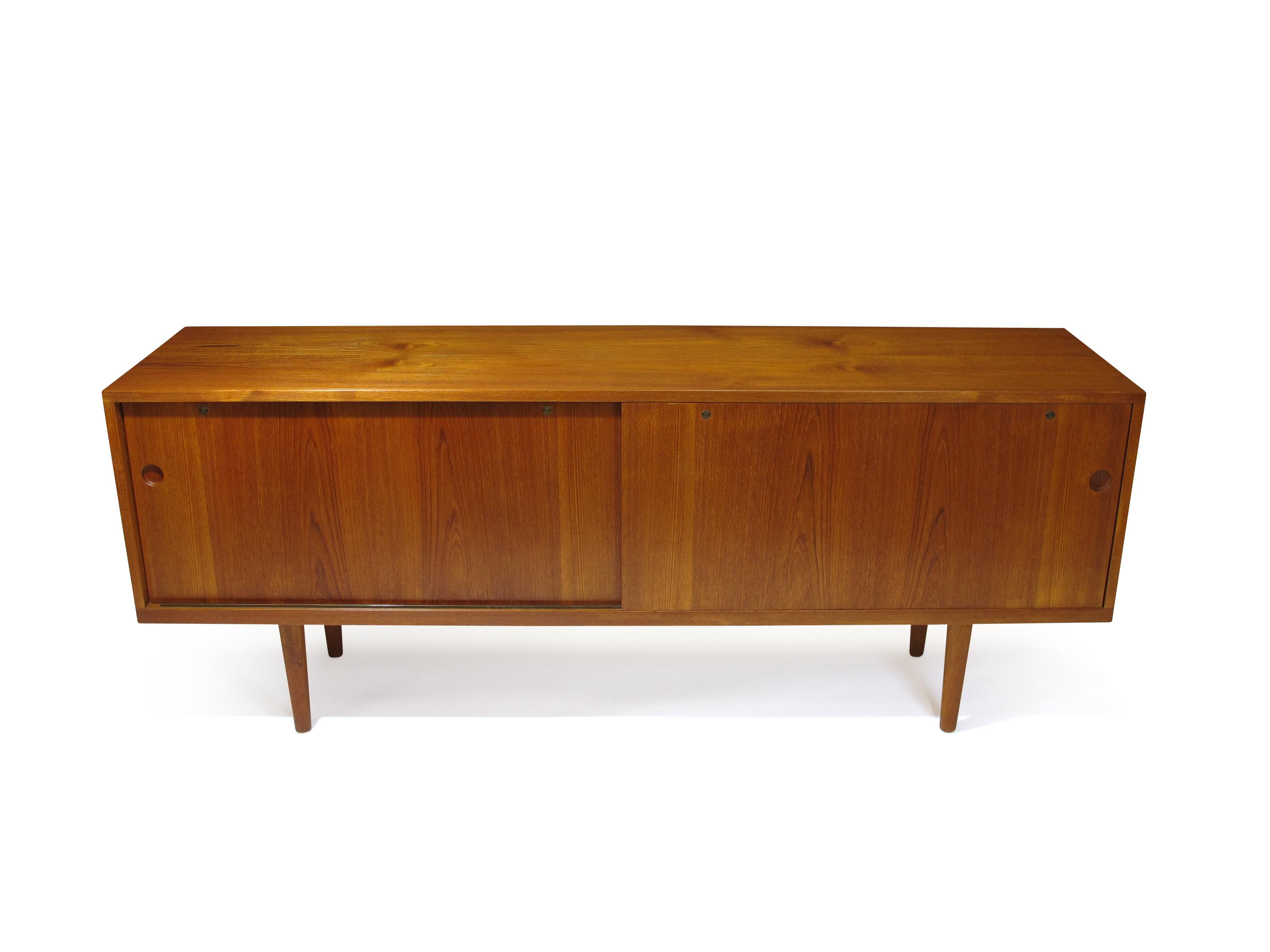 Sideboard designed by Hans Wegner for Ry Mobler, model 26. Minimal design with two sliding doors revealing an interior of white oak with adjustable shelves and silverware drawers; raised on round tapered teak legs. The cabinet has been