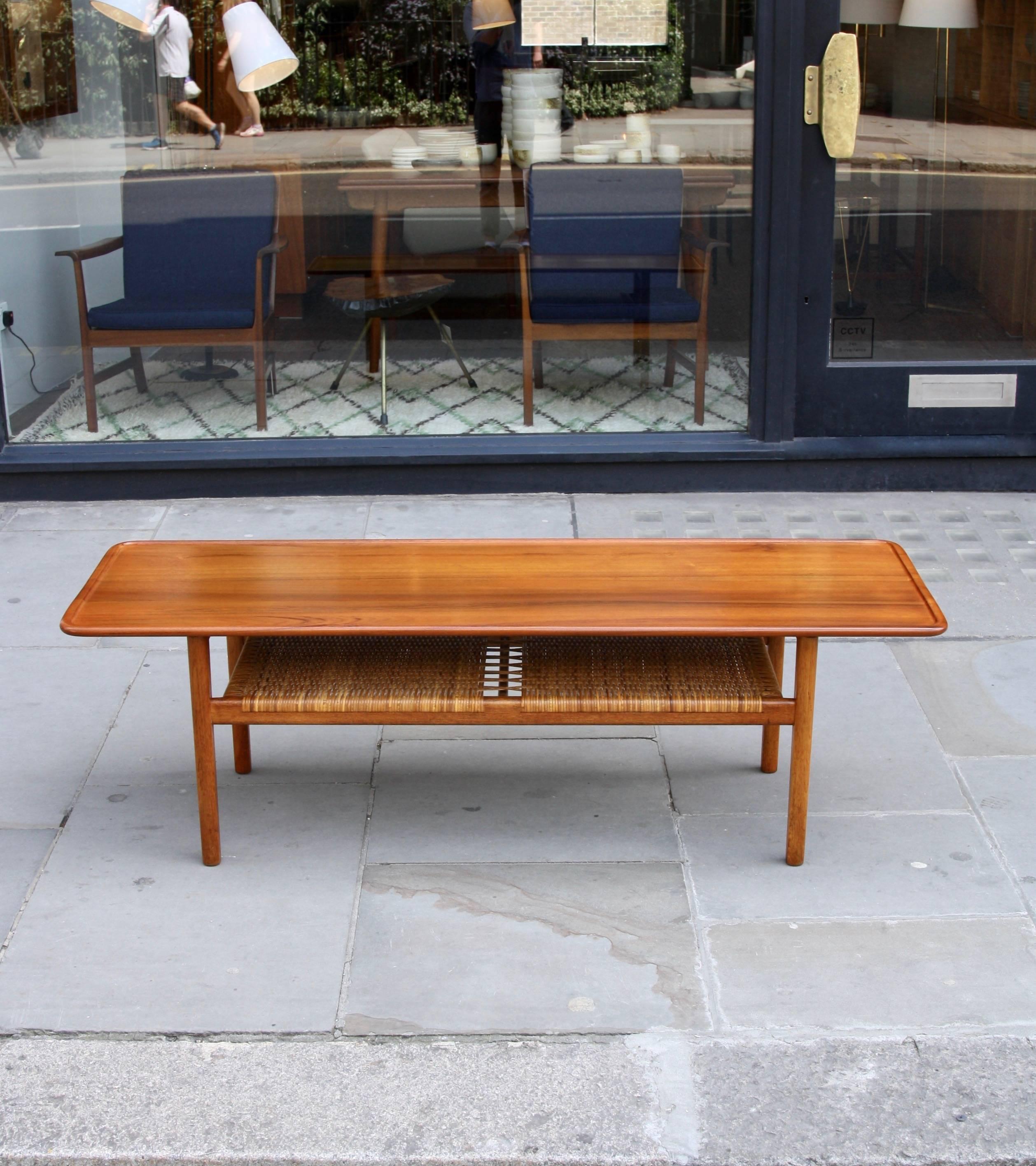 A vintage model AT-10 lounge table designed by Hans Wegner for Andreas Tuck in 1955. 

The narrow but long table top is carved from solid teak and features a deep routed edge which forms a lip to the parameter of the table. The undercarriage is