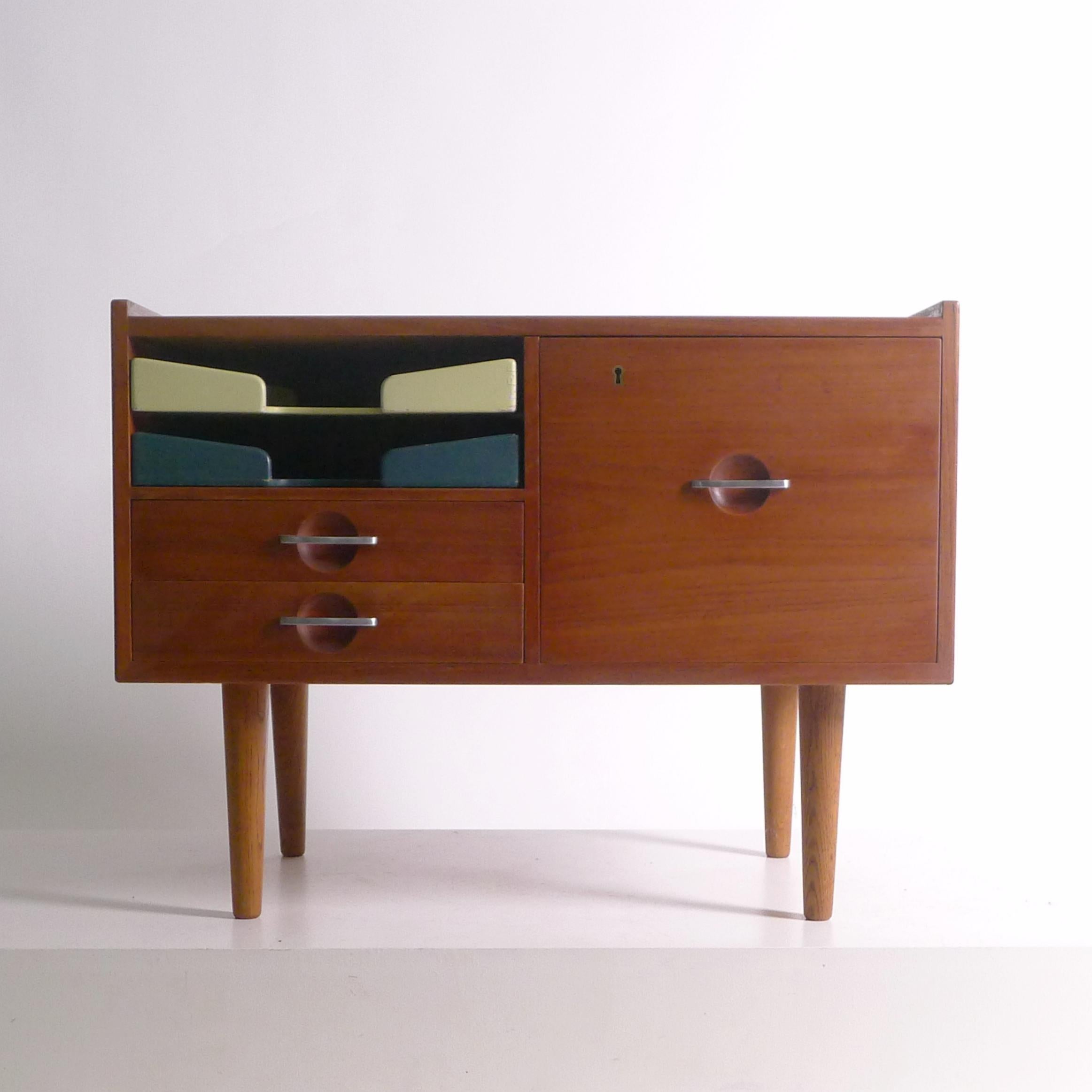 Hans J Wegner 
Telephone Table, designed 1954
made by Johannes Hansen in the 1950s, stamped
teak cabinet in with black laminate top on turned oak dowel legs, fitted two painted wood paper trays to the left side above two drawers and a larger 