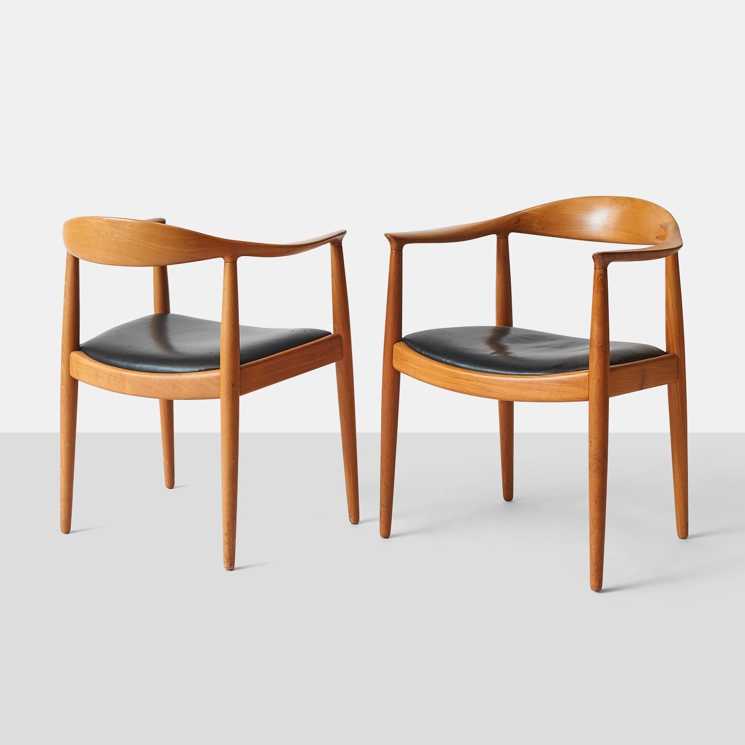 A pair of oak armchairs featuring an inset black leather seat, each having a shaped crest above a black leather seat and tapered legs.

Hans J Wegner 