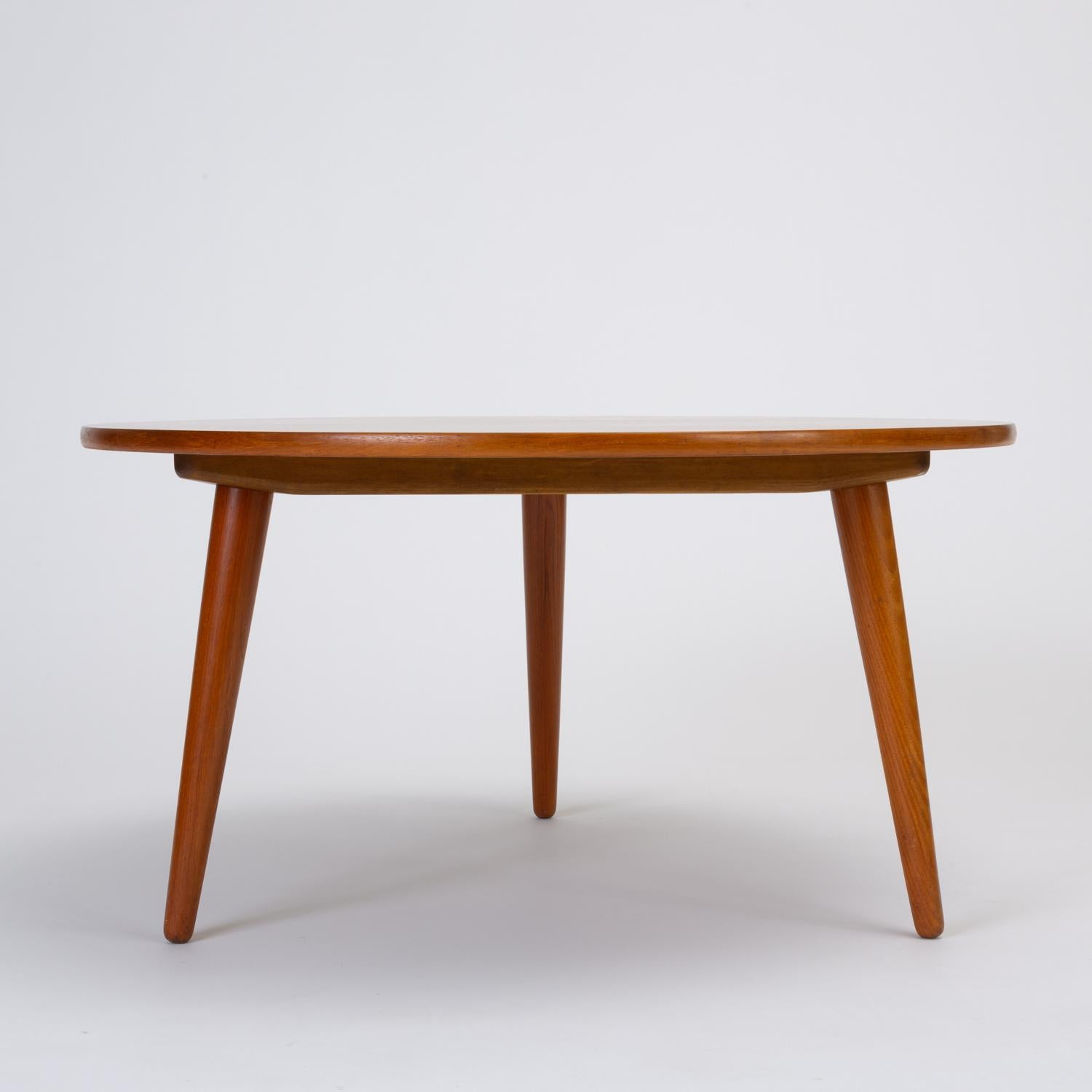 Designed by Hans Wegner in 1954 for Andreas Tuck, the AT-8 coffee table has a round teak surface and sits on three tapered dowel legs of solid teak. The oak apron beneath the table is stamped with the Andreas Tuck/Hans Wegner manufacturer's mark.