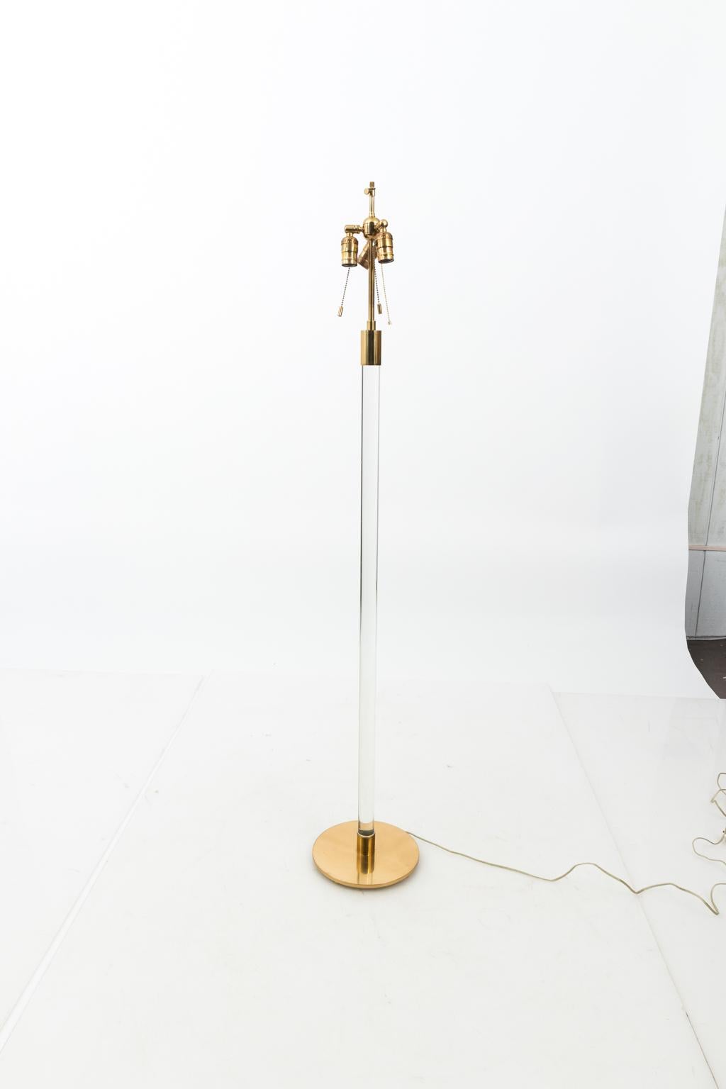 Hansen and Company tubular Lucite floor lamp with round brass base, circa 1975. Linen drum shade is not included. The lamps can adjust from 60.00 inches to 65.50 inches tall. Please note of wear consistent with age along with minor oxidation to the