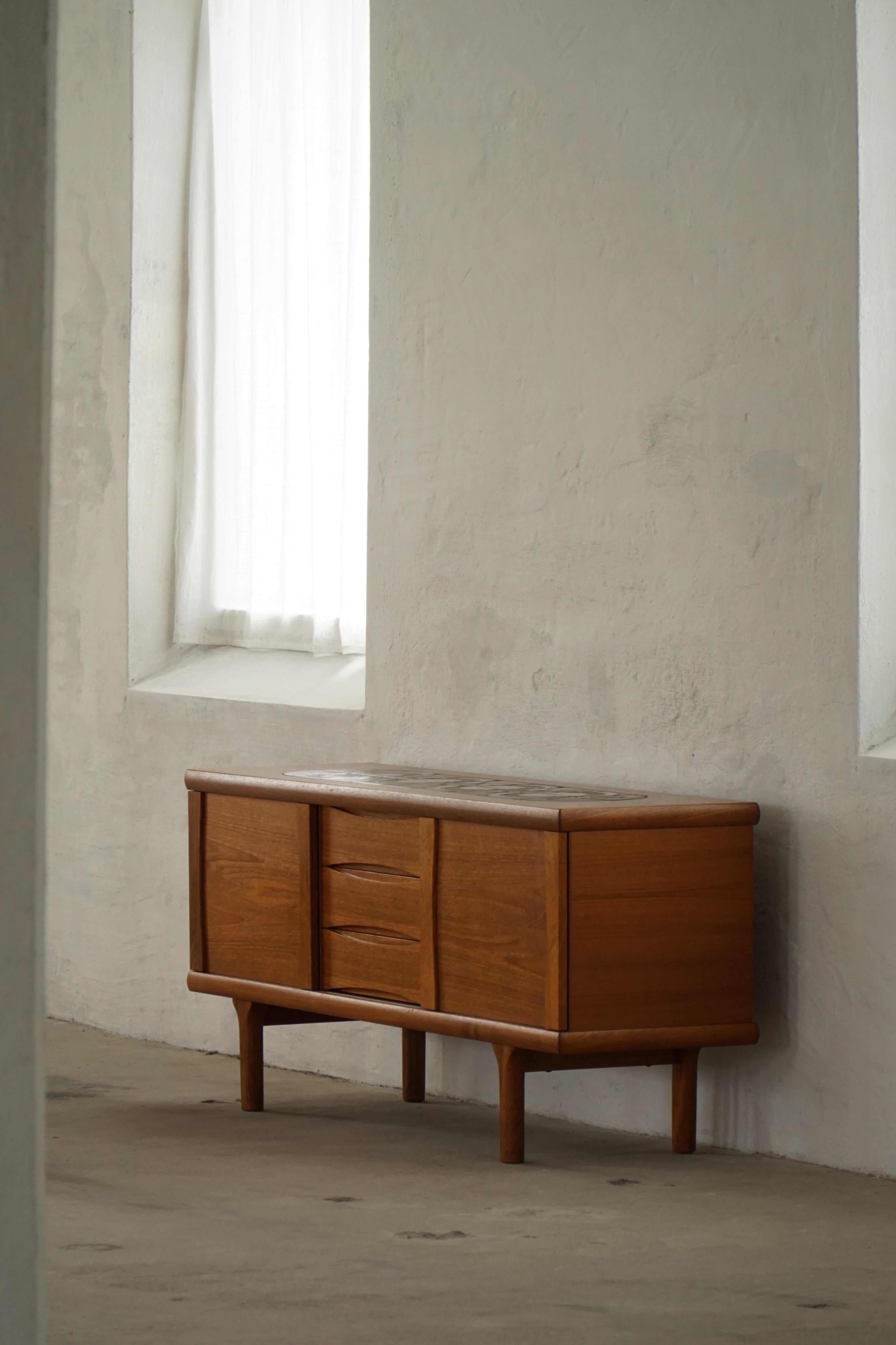 Superbe buffet / crédence autoportant de style moderne danois par Hansen & Pedersen, fabriqué dans les années 1960 en bois de teck riche et chaleureux. La pièce comporte des portes coulissantes avec des poignées de forme organique, trois tiroirs
