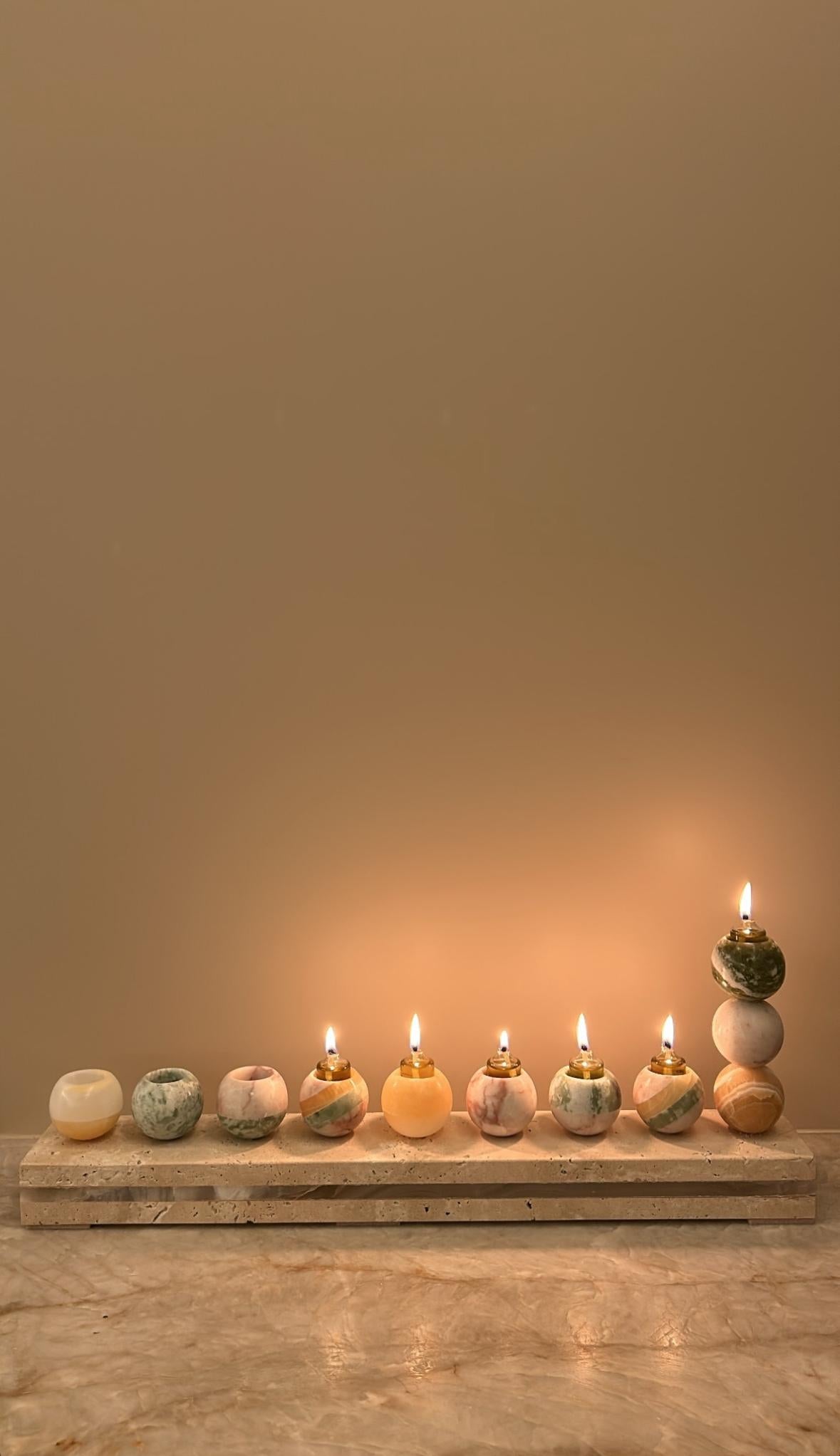 Esta Hanukkiah escultórica de Studio Gaïa reinterpreta el espíritu de Hanukkah a través de una lente contemporánea, mezclando ónice multicolor y travertino natural con notable precisión artesanal.
Cada una de las nueve esferas, talladas a mano en