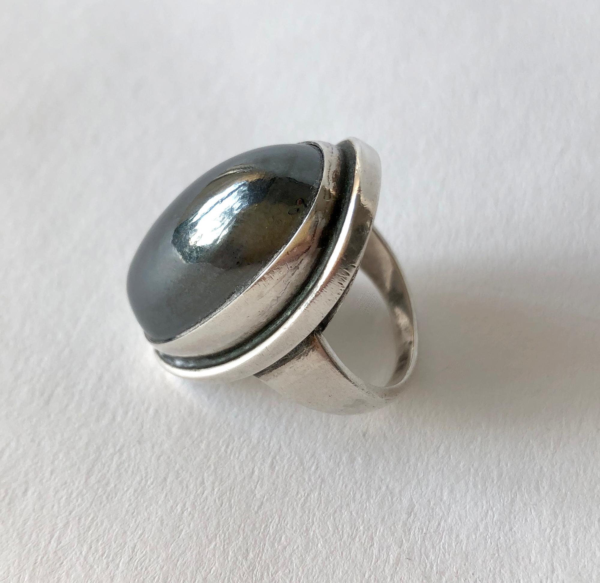 Hematite cabochon stone set in sterling silver ring designed by Harald Christian Nielsen for Georg Jensen, circa 1950.  Ring is a finger size 8.25 and is signed Georg Jensen, 46E, Denmark. In very good vintage condition.

Neilsen was a Danish