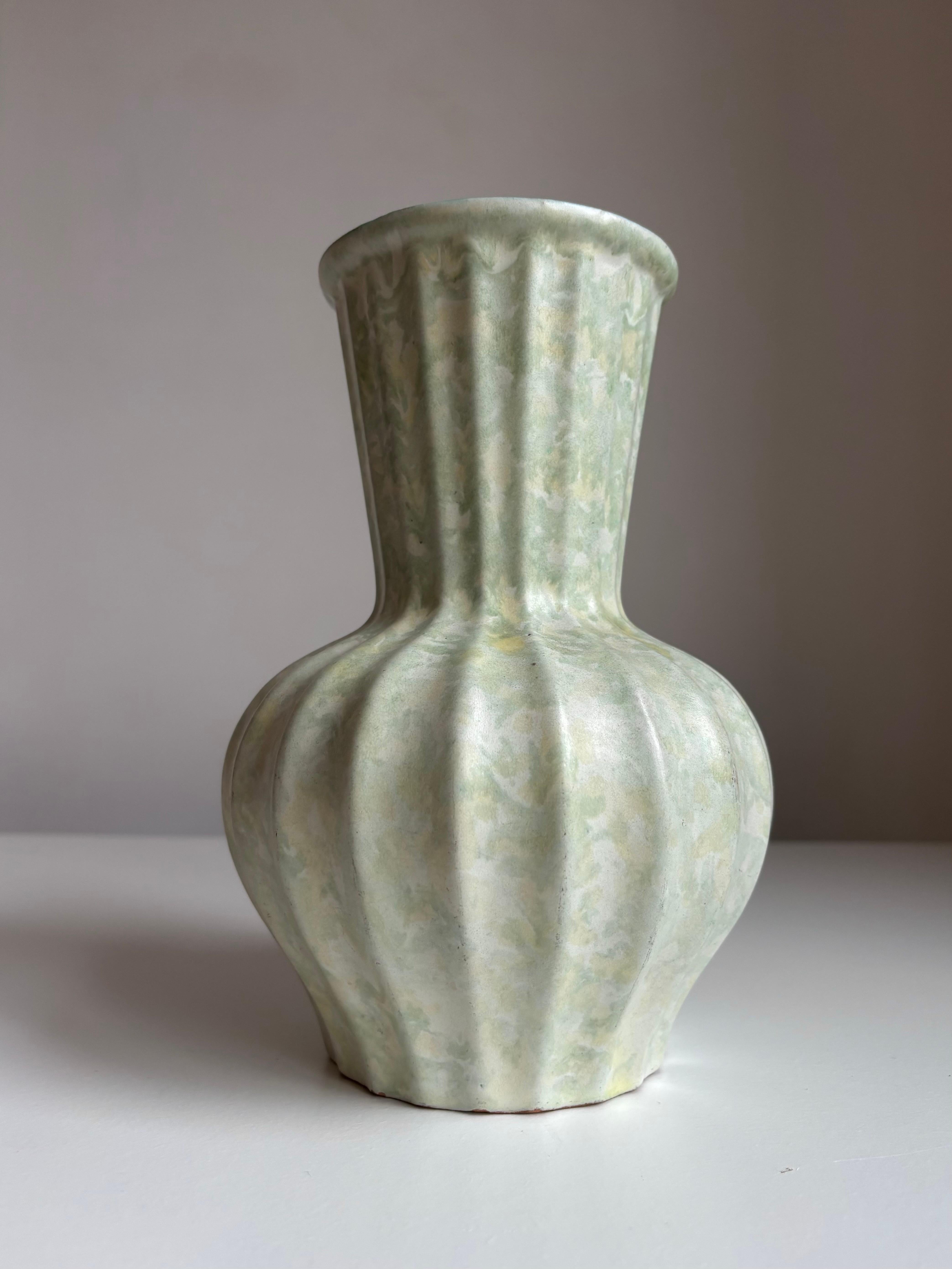 Jarrón de loza art decó esmaltada en mármol con forma de ánfora y cuerpo estriado horizontalmente. Realizado por el ceramista Harald Östergren para Upsala Ekeby en la década de 1930. Esmalte de mármol verde menta, blanco y amarillo. 
Precioso estado