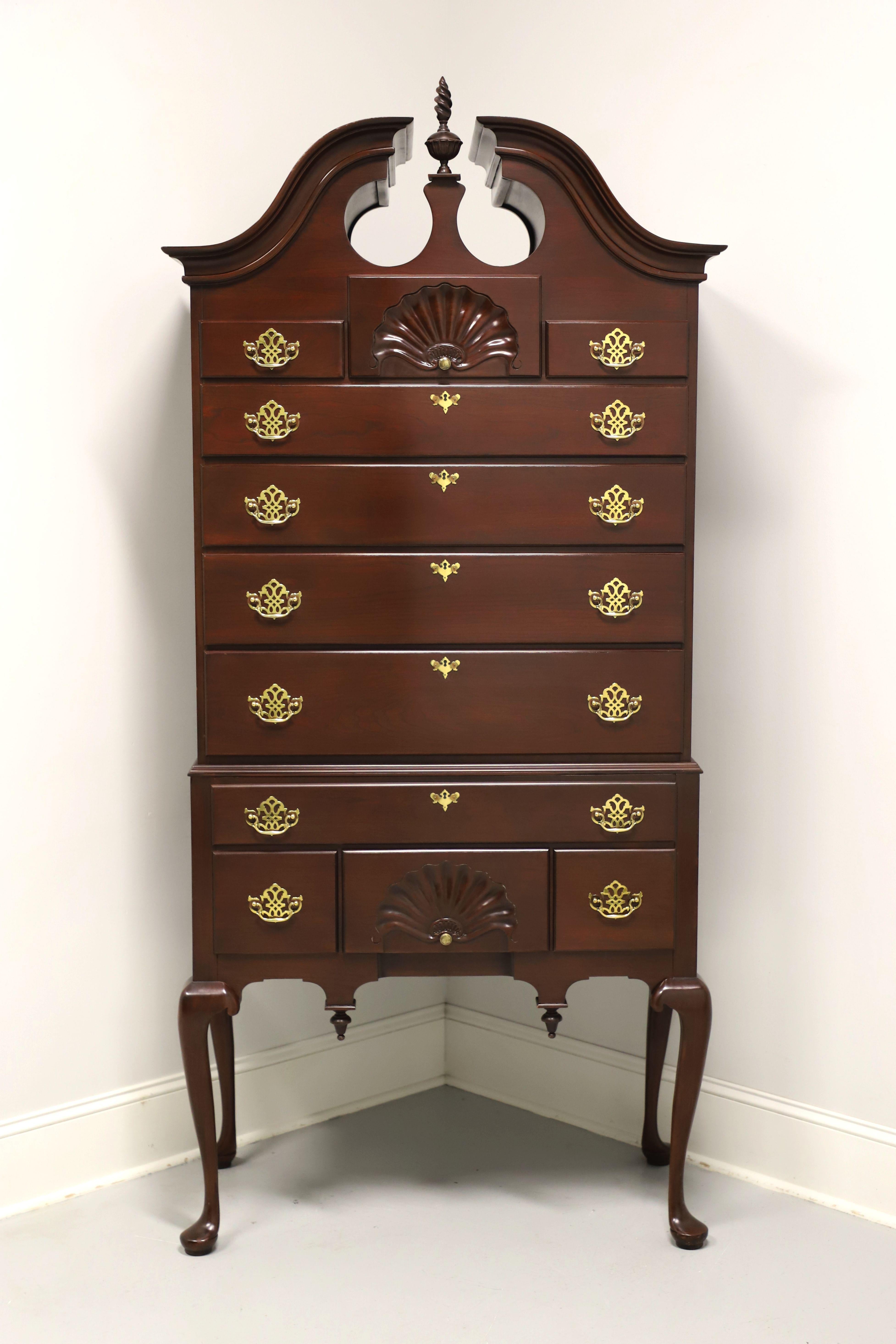 A Queen Anne style highboy chest by Harden Furniture. Solid cherry wood with brass hardware, complimented by broken bonnet top, flame form center finial, shell carvings, carved apron with decorative reverse finials, and raised on tall cabriole legs