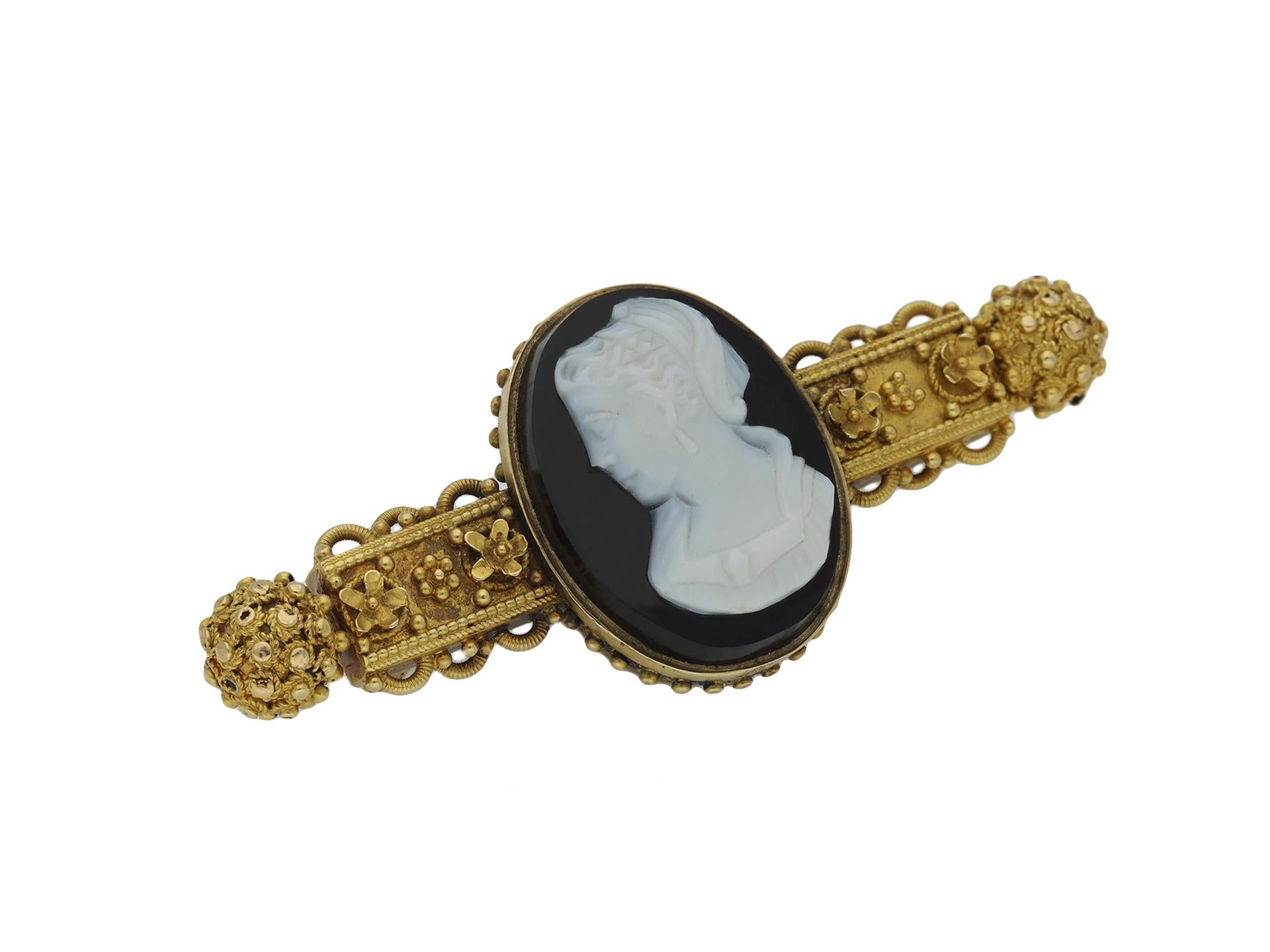Hardstone cameo brooch. Set with a carved hardstone cameo to centre of a bust of a lady in profile within a yellow gold ornate horizontal form, with gold wirework, floral beading and terminating with two circular clusters. Fitted with bar and