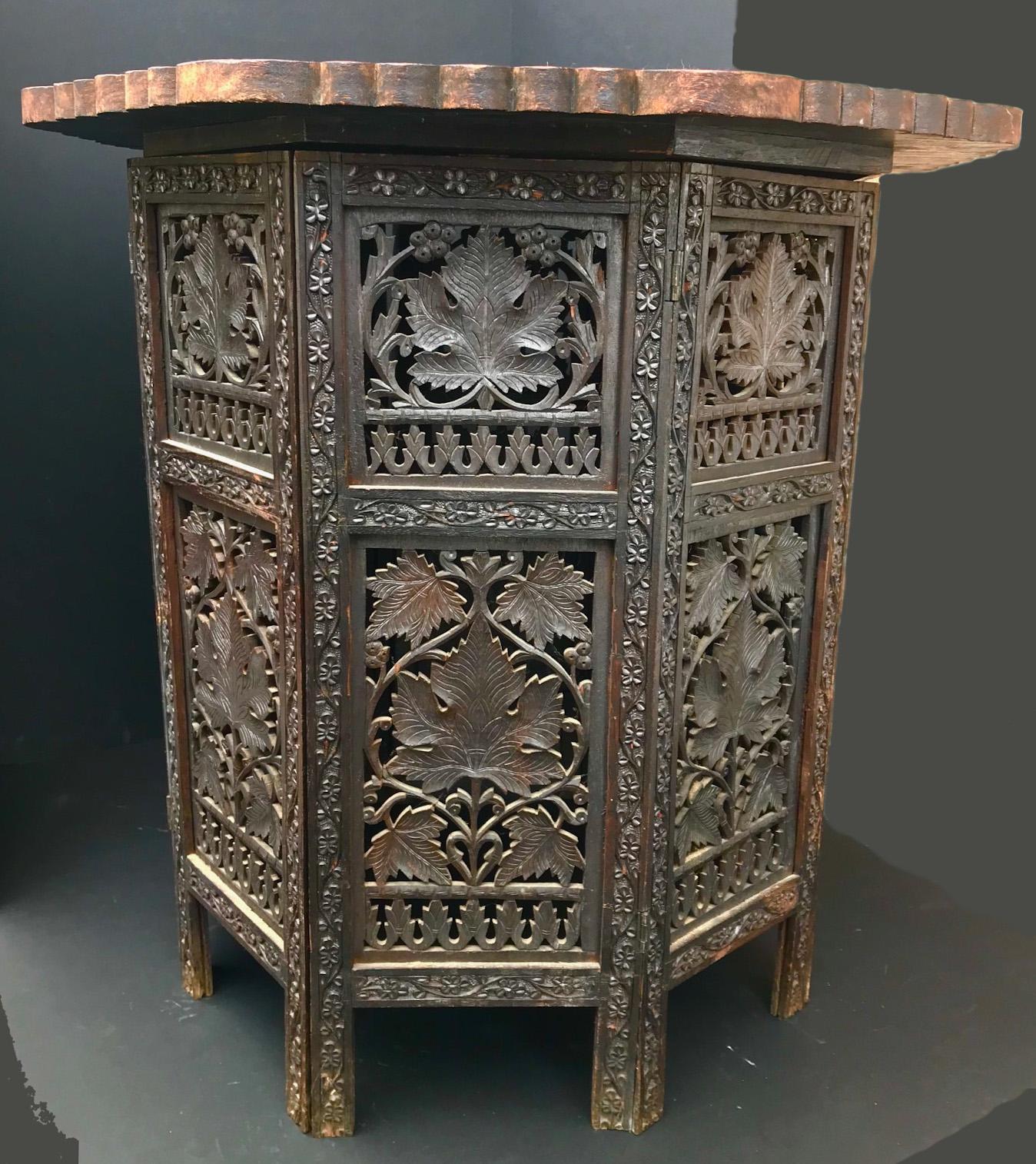 This octagon hardwood Tabouret is intricately carved with grape vine leaves. The top is highly decorated with a carved design and the center is inlaid with brass ornaments. The top is removable and the hinged base can be folded flat. This side table