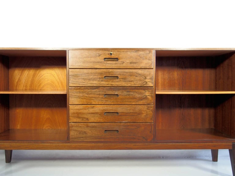 Scandinavian Modern sideboard with slanted legs designed by Kai Winding. Five drawers with a lock on the top one, keys included. Two doors behind which are shelves. Back of wood veneer, labelled Danish furniture makers control.