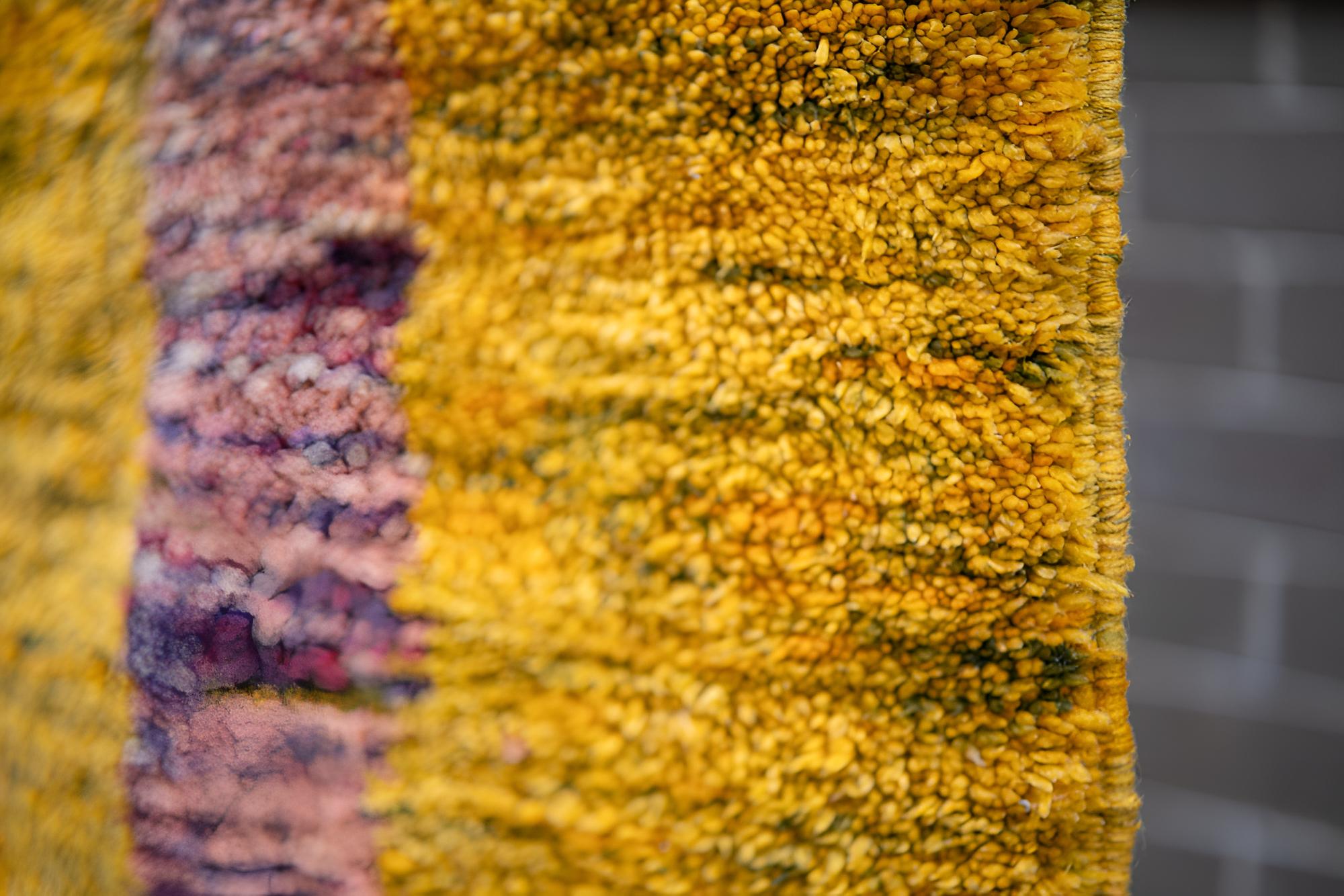 Dieser handgefertigte Nepalteppich zeigt ein atemberaubendes Zusammenspiel von Erdtönen und symbolischer Abstraktion. Der reiche Hintergrund in goldenem Ocker bildet eine warme, erdende Basis, während die zentralen Motive - in sanften Mauve-,