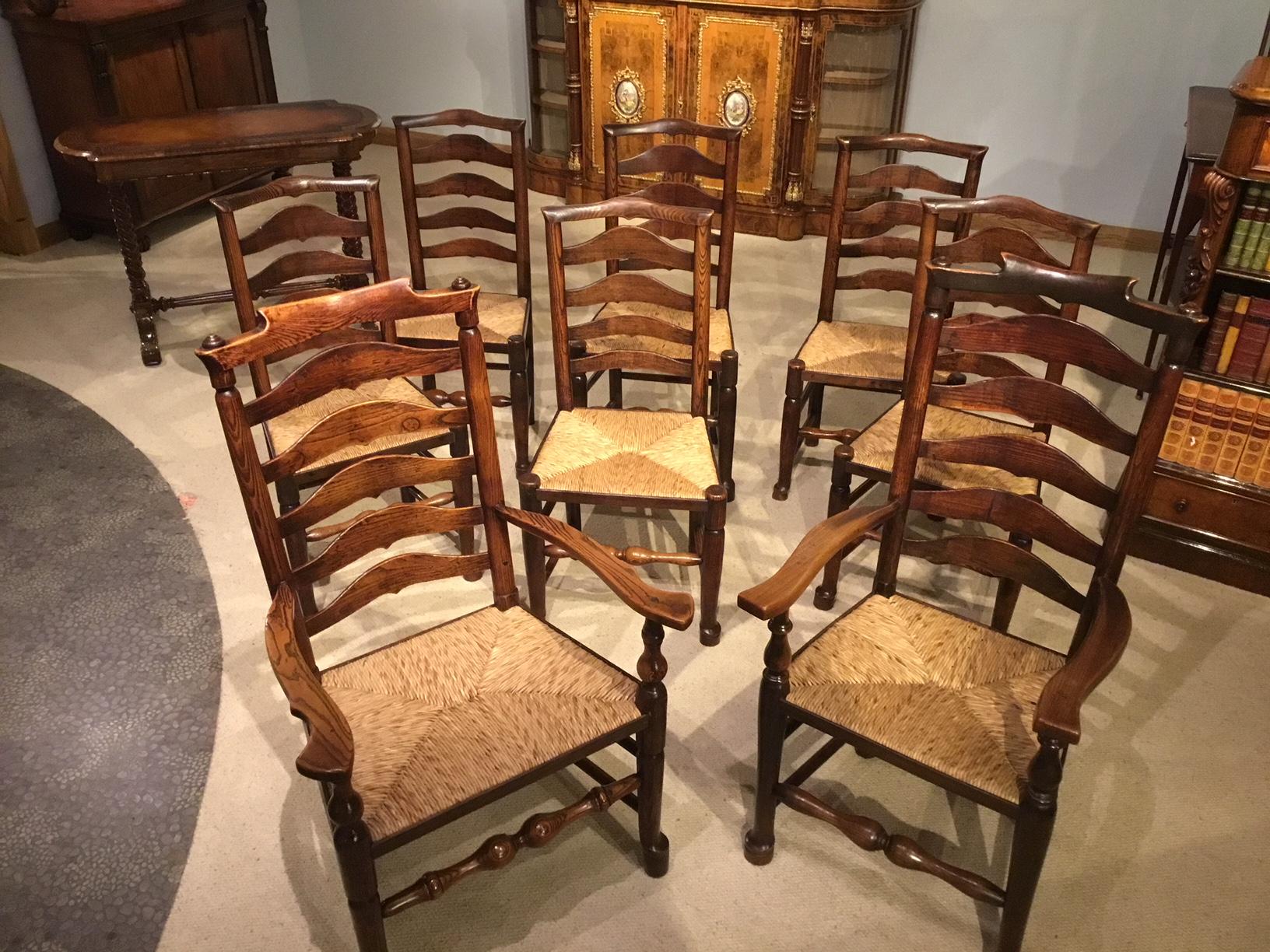 A harlequin set of 8 early 19th century ash and elm ladder back kitchen dining chairs. The carver chairs with six ladder backs, open arms, rush seats, raised on turned supports with pad feet and united by rolling pin front stretchers. The stand