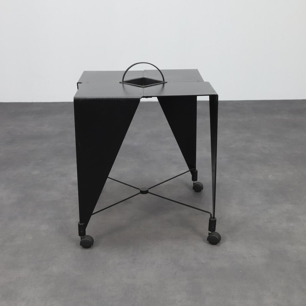 Llamativa y angulosa composición en chapa de acero, esta mesa auxiliar de Errebi refleja el lenguaje gráfico y expresivo del postmodernismo italiano de los años 80. Las patas afiladamente plegadas y la parte superior pentagonal recortada forman una