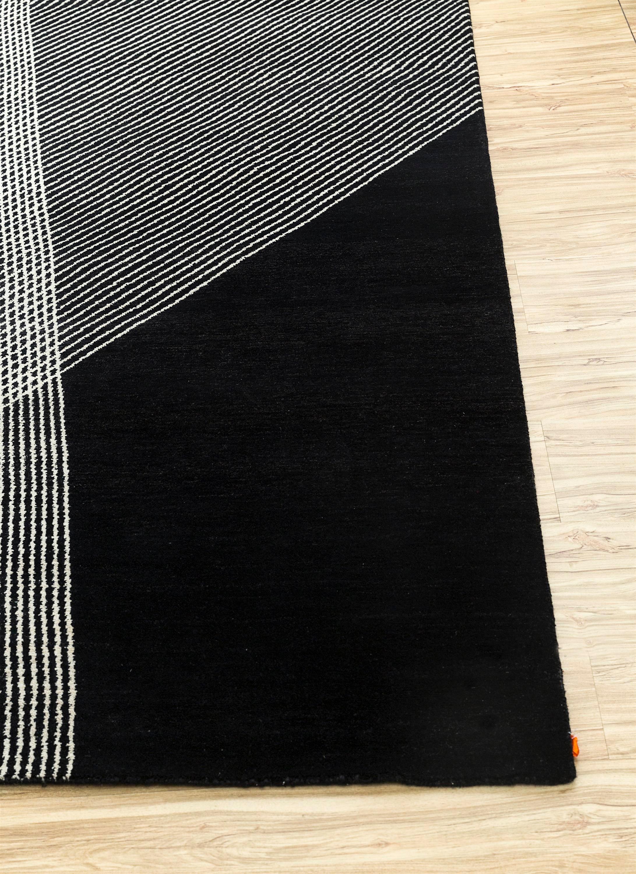 Seeking a geometric rug that transcends ordinary design? Explore the extraordinary with this Hand-Knotted Rug. Handmade in rural India, it showcases a captivating play of color blocks and symmetric lines. The ground color, an enticing ebony,