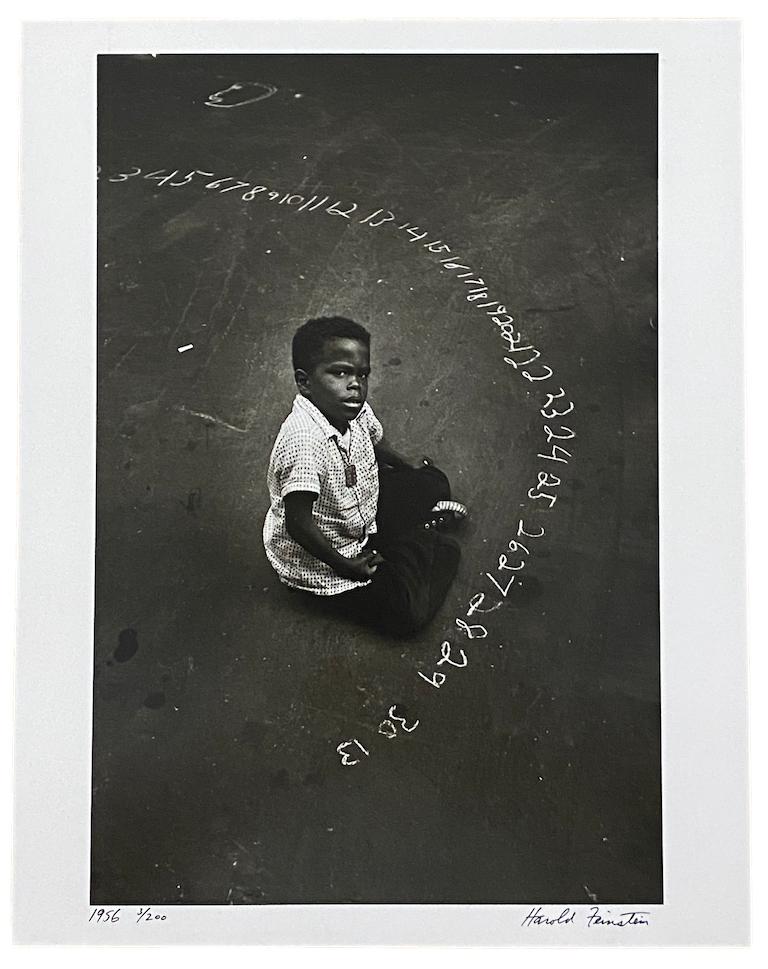 Boy with Chalked Numbers, NYC by Harold Feinstein is a 14 x 11 inch gelatin silver print, and is edition 3/200. This photograph features a boy sitting on the ground, surrounded by numbers written in chalk on the ground. This photograph is signed,